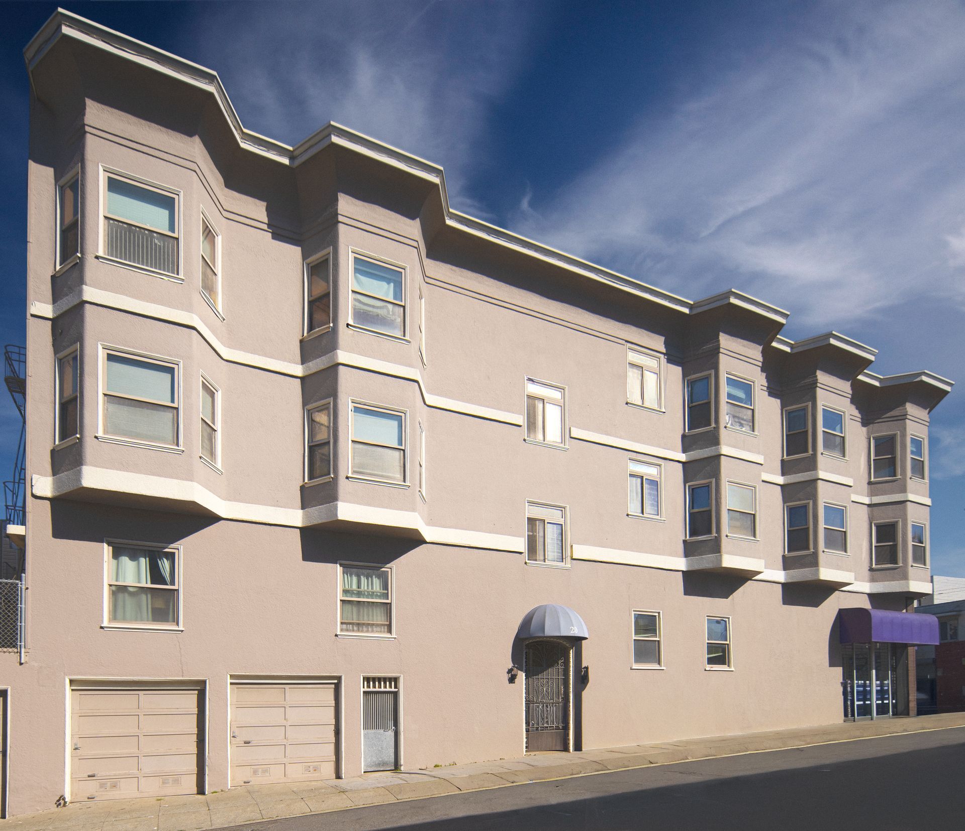 Two-story building with balconies, basketball hoop, and green lawn.