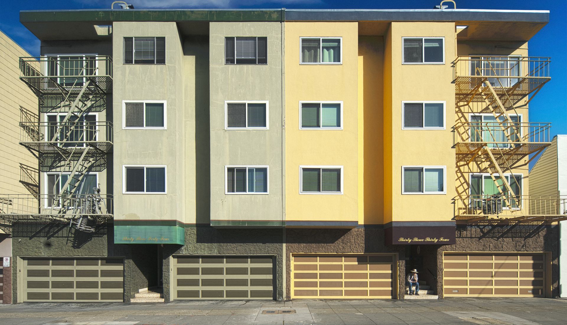 Multi-story apartment building with garage doors, in shades of gray and yellow.