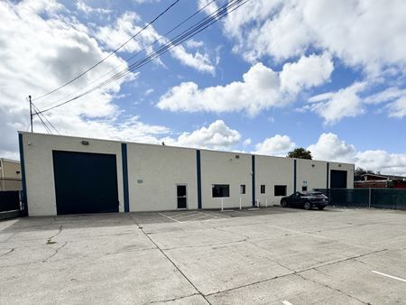 Warehouse building with blue doors and a parked car under a cloudy sky.