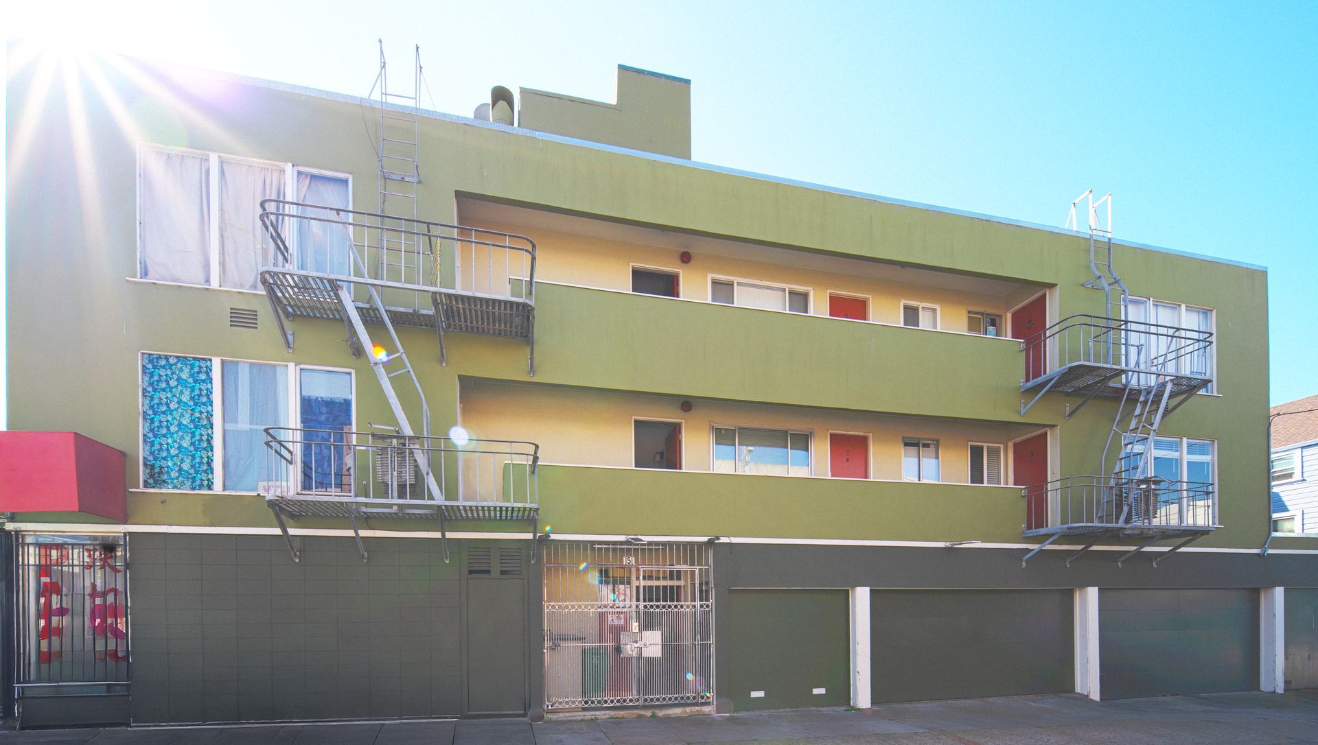Building with a red-signed business on the ground floor, beige and gray walls, and parked car on a city street.
