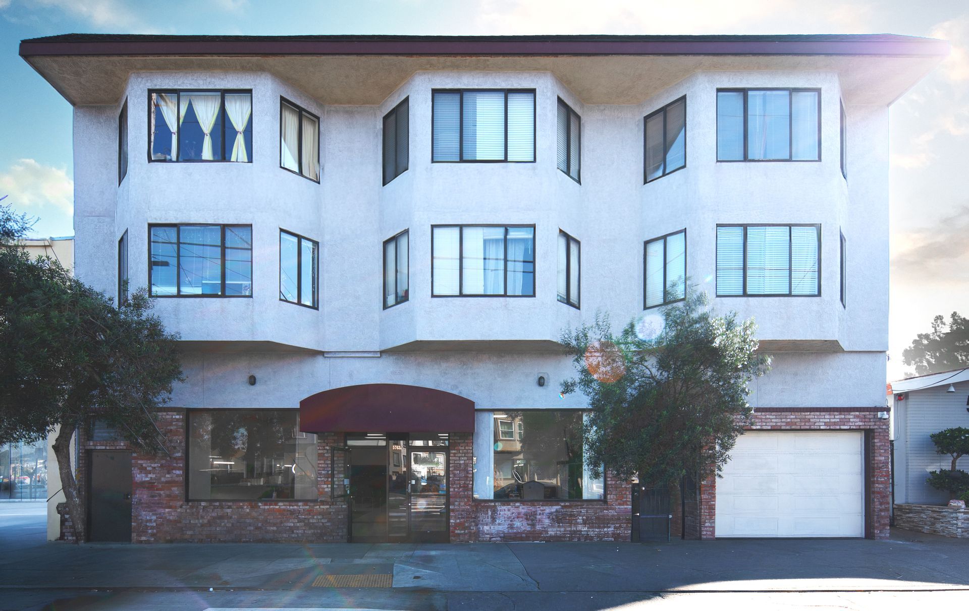White three-story building with dark-framed windows, brown awning, and blue sky.