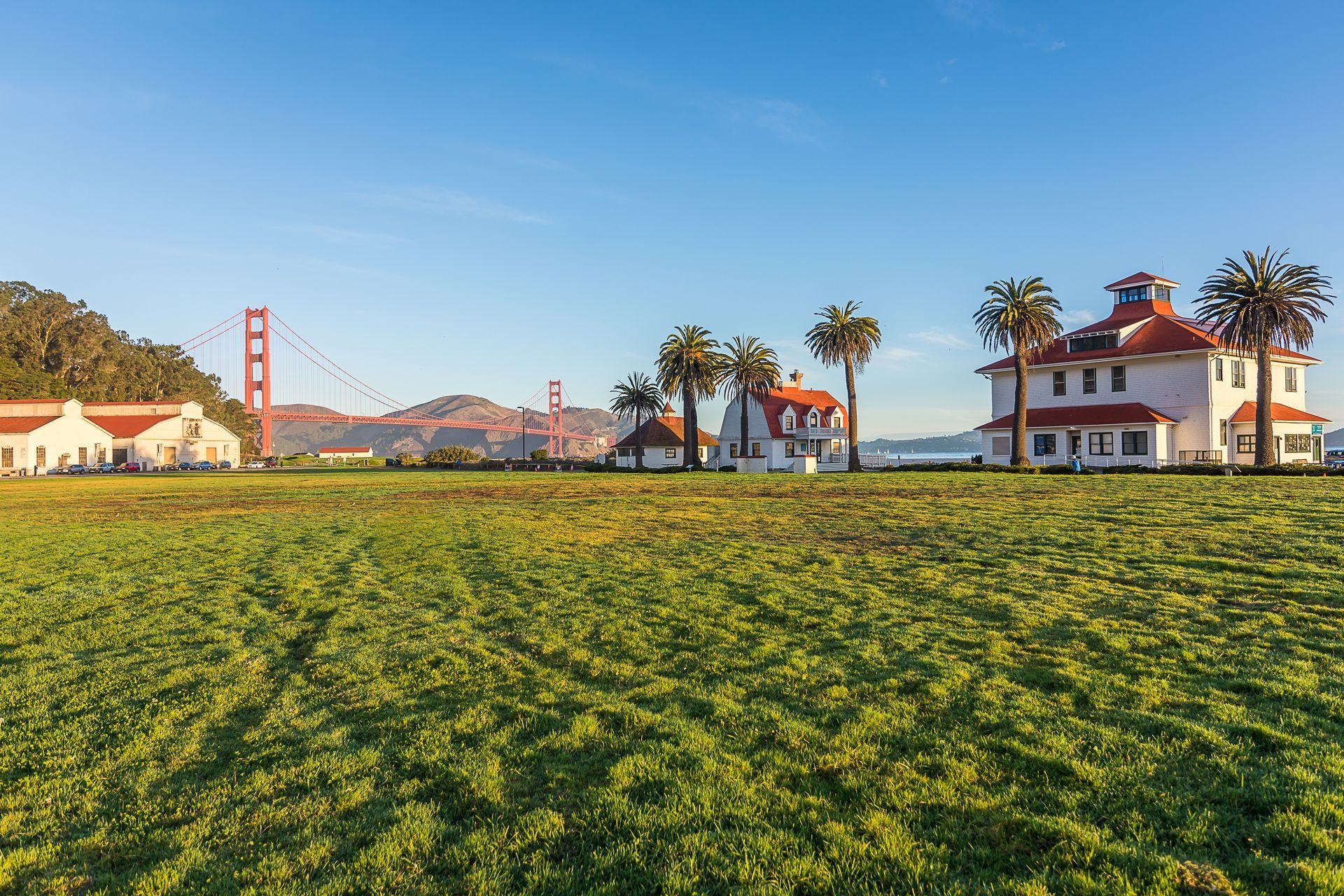 Green field with buildings and Golden Gate Bridge in the background, under blue sky.