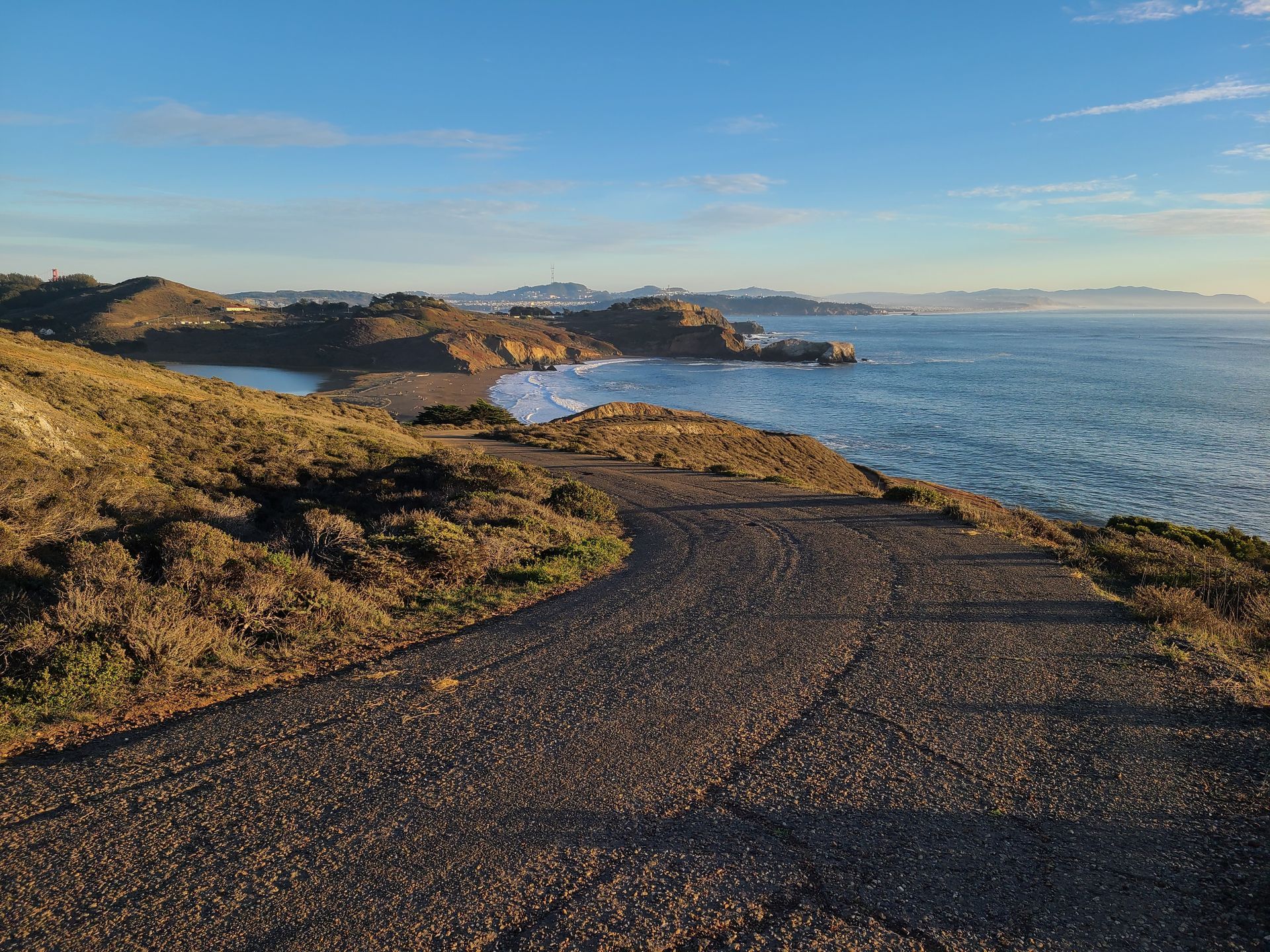 Coastal path overlooking ocean and rocky coastline under a blue sky.