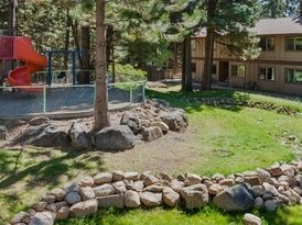 Playground with a red slide, surrounded by a rock wall, in front of a two-story building.