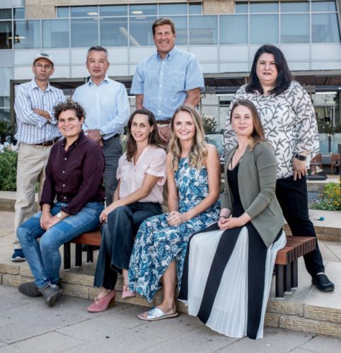 Group of people posing outdoors; building in background. Some seated.