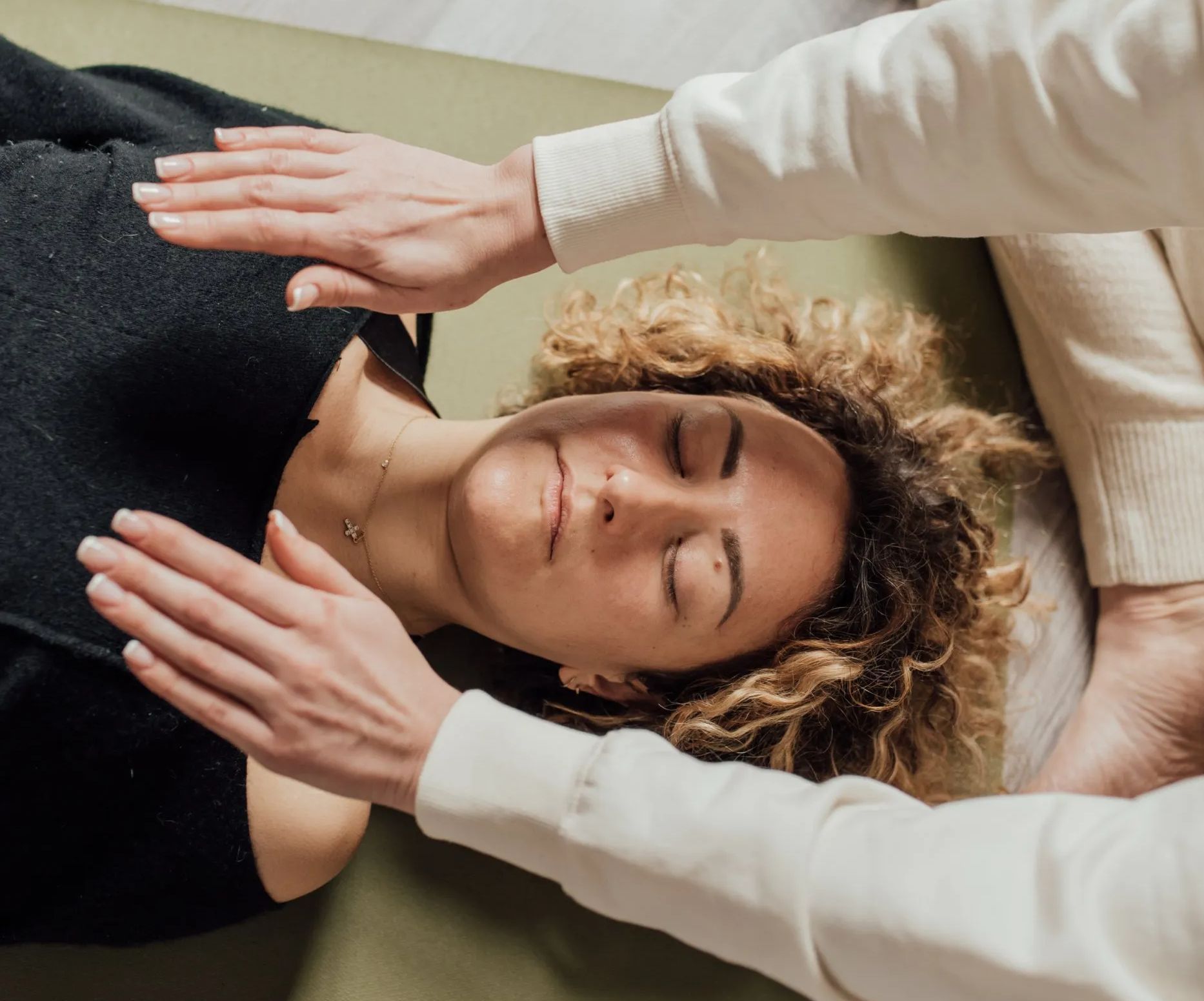 A woman is laying on a bed with her eyes closed while a man holds her hands over her head.