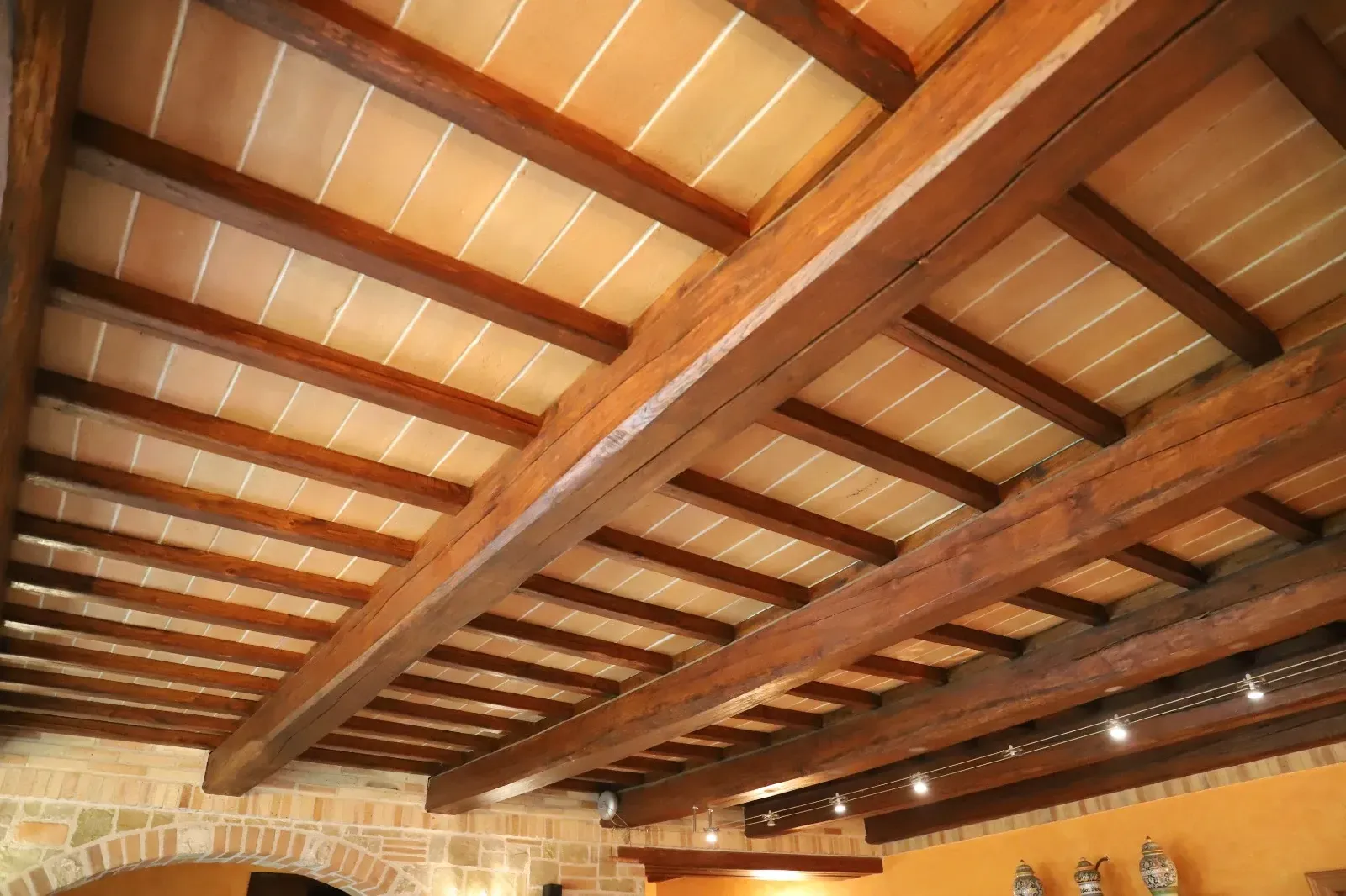 Soffitto con travi in ​​legno, piastrelle in terracotta e pareti in pietra in un interno rustico.