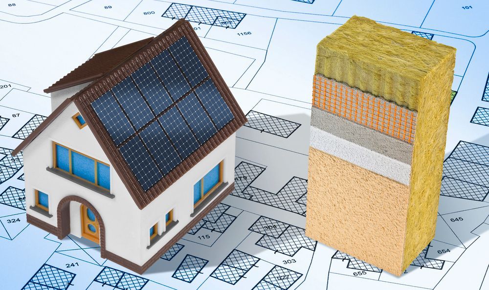 Modellino di casa accanto a un campione di parete a strati su planimetrie, che illustra la costruzione e l'isolamento di un'abitazione.