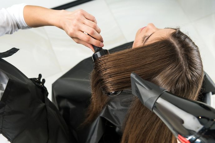 Parrucchiere applica la tinta ai capelli castani di una cliente con pennello e stagnola al lavandino del salone.