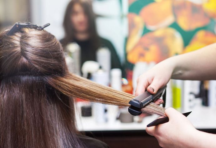 Una parrucchiera usa una piastra su lunghi capelli castani davanti allo specchio di un salone.