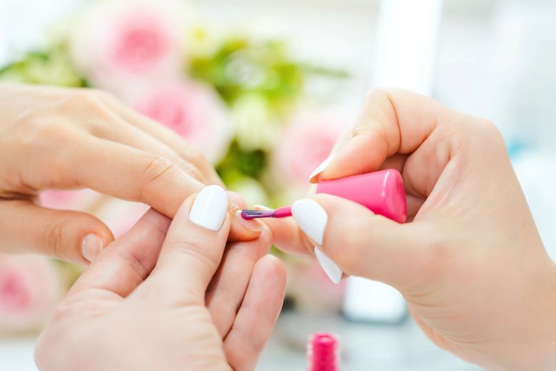 Mani che applicano smalto rosa sulle unghie in un luminoso salone di bellezza.