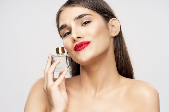 Donna con rossetto rosso e un leggero sorriso, che tiene una boccetta di profumo vicino al viso, su sfondo bianco, su sfondo bianco.
