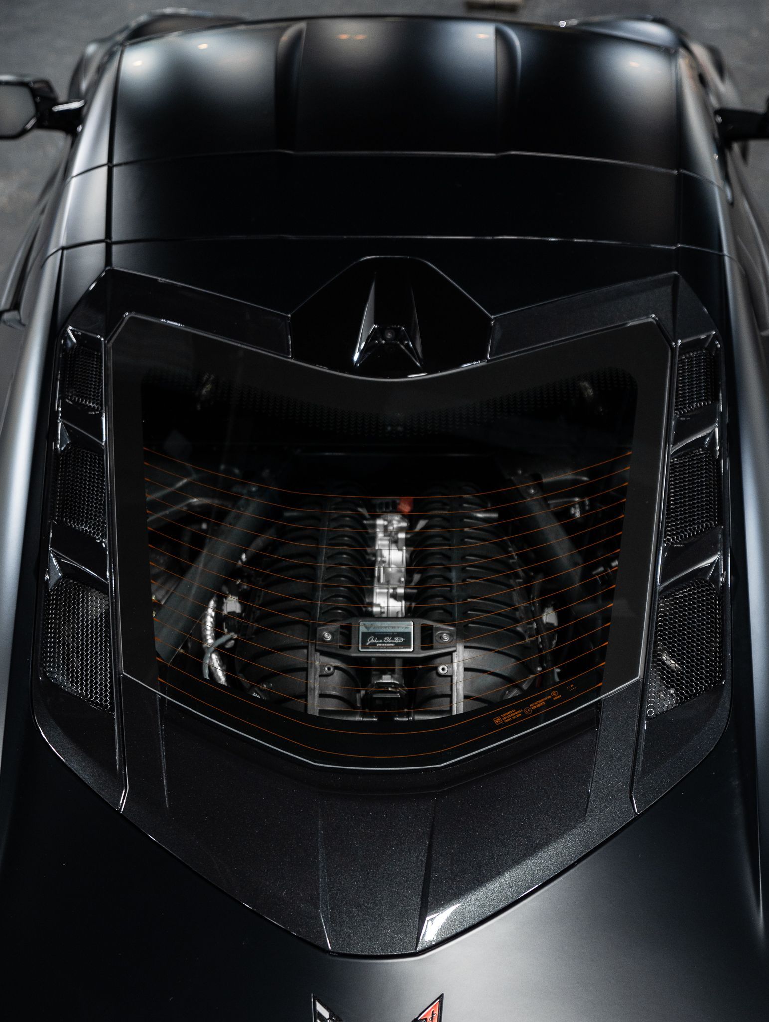 Top-down view of a black sports car's mid-engine visible through a carbon fiber rear window hatch.