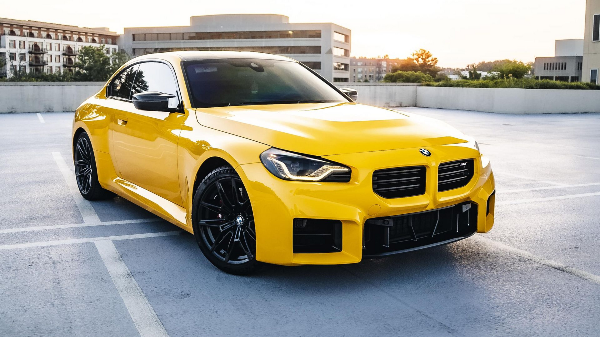 Yellow BMW coupe parked on a rooftop. Black wheels and trim. Rear view.