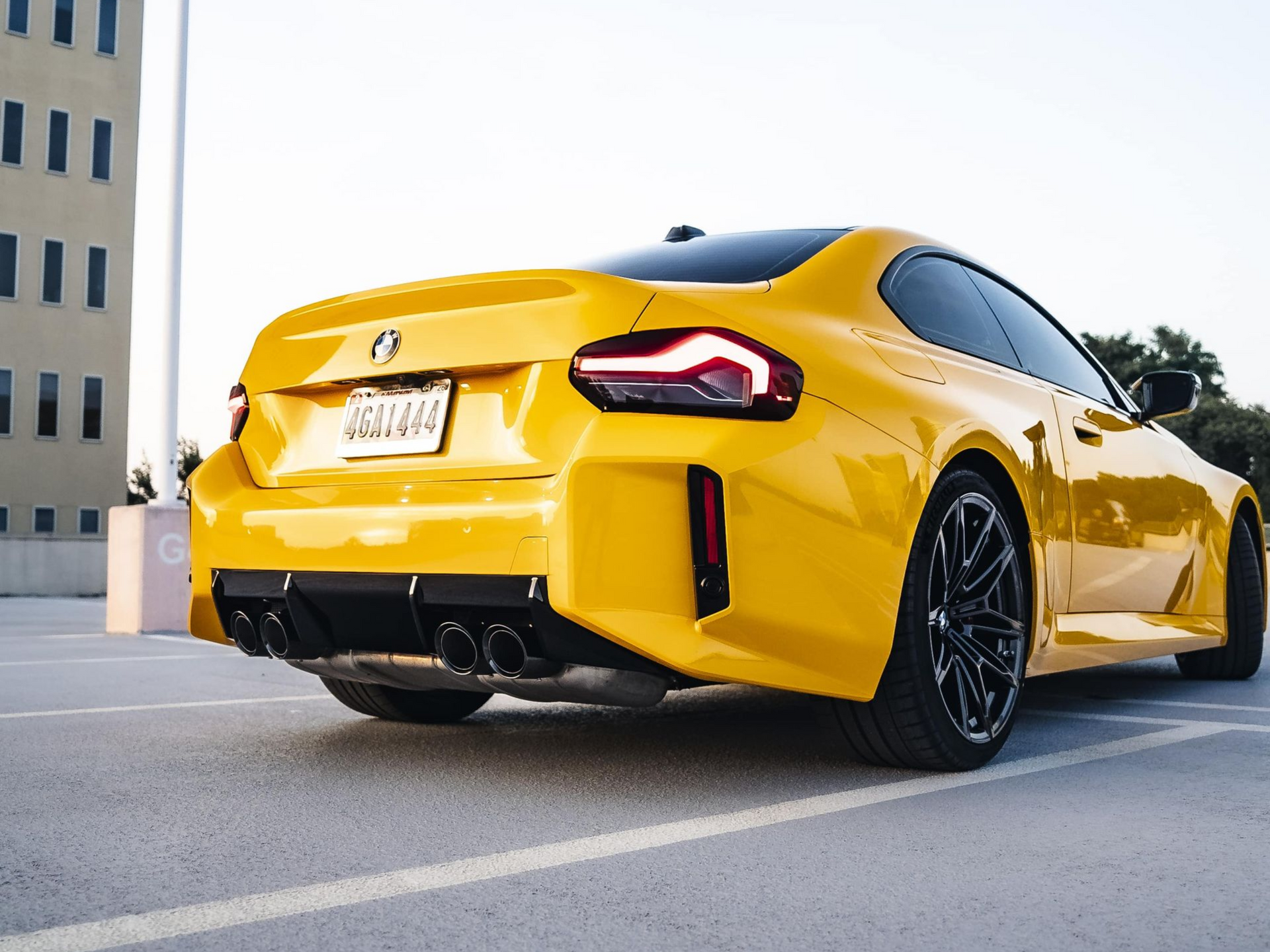 Yellow BMW coupe parked on a rooftop. Black wheels and trim. Rear view.
