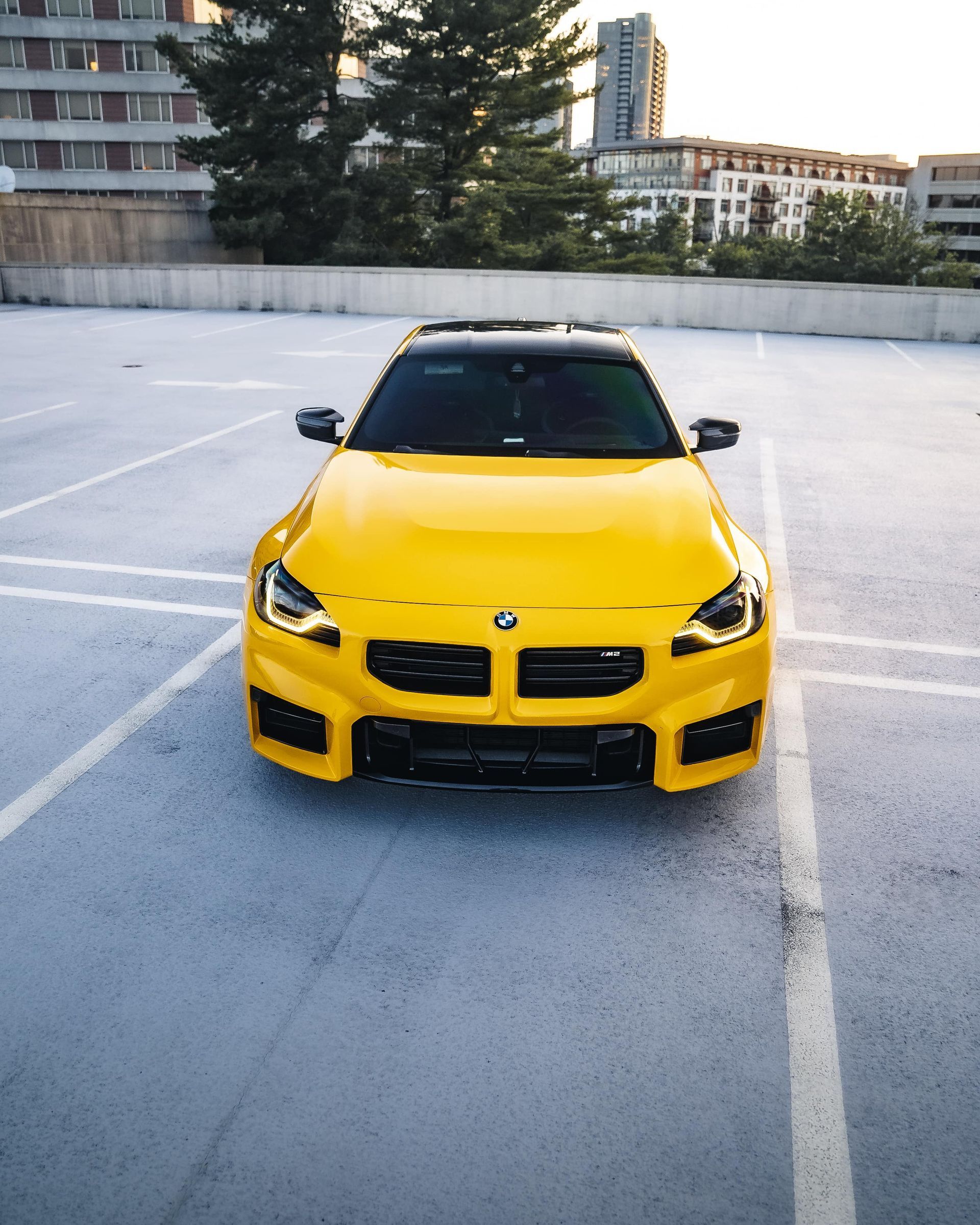 Yellow BMW car parked on a rooftop parking lot with a cityscape in the background.