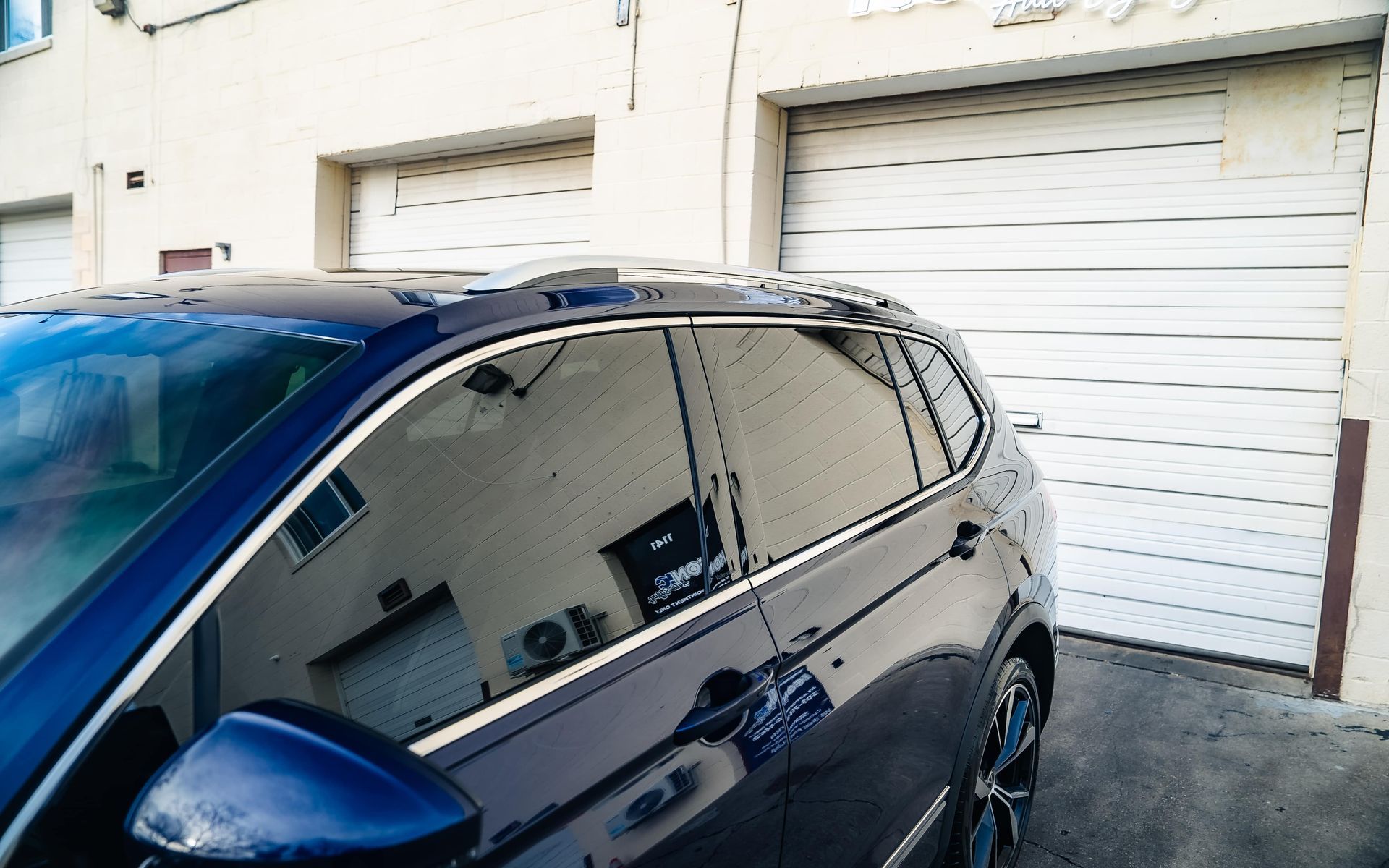 Dark blue SUV parked near a white garage door, reflecting the building and sky.