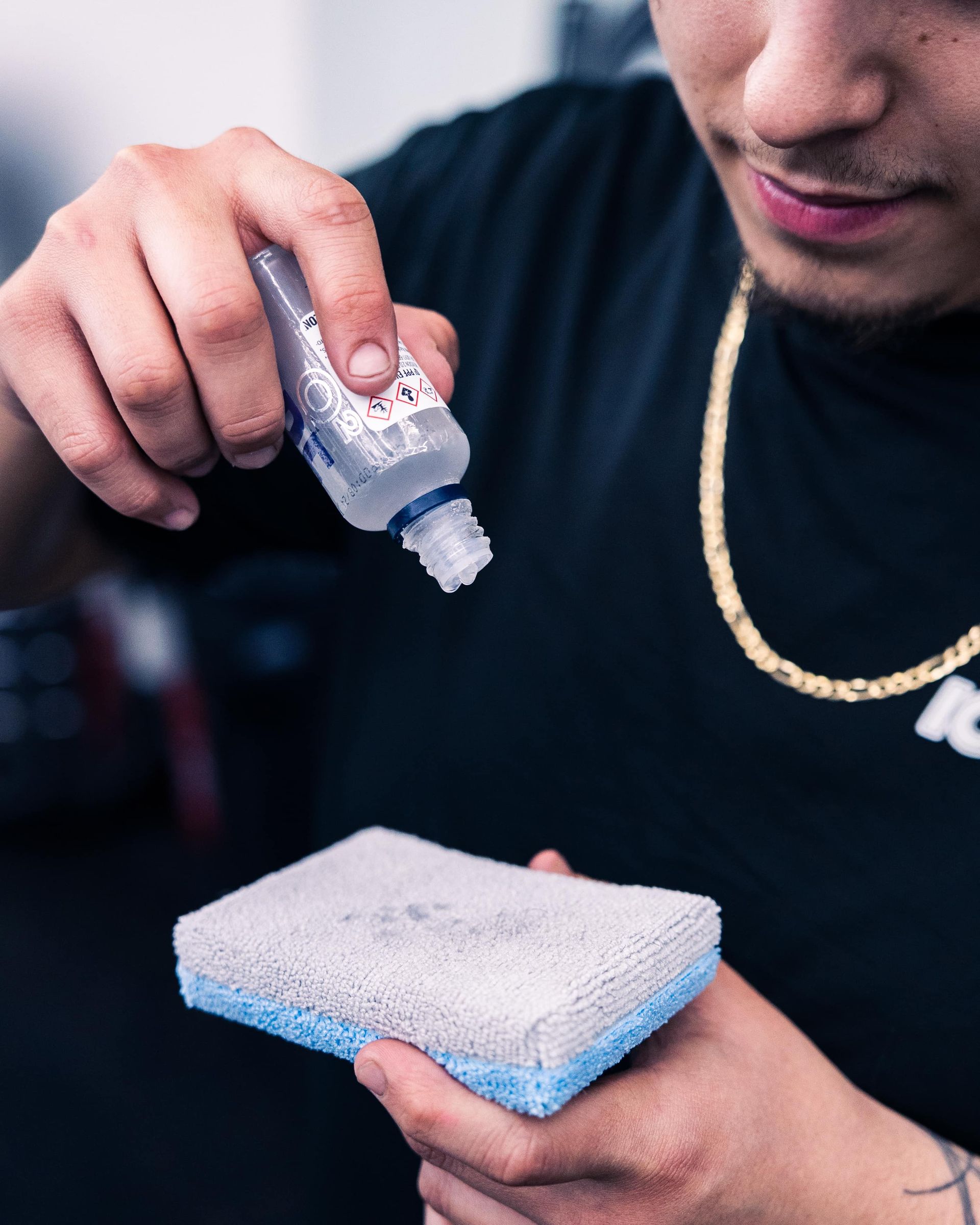 Person squeezing liquid from a bottle onto a blue-edged sponge.