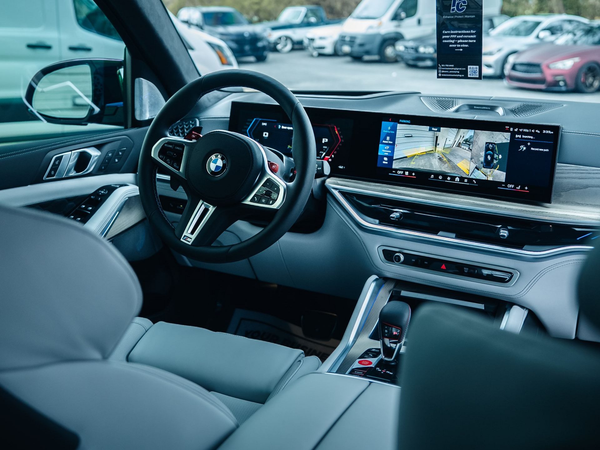 Interior view of a modern BMW car featuring a digital curved display, black steering wheel, and light grey leather seats.