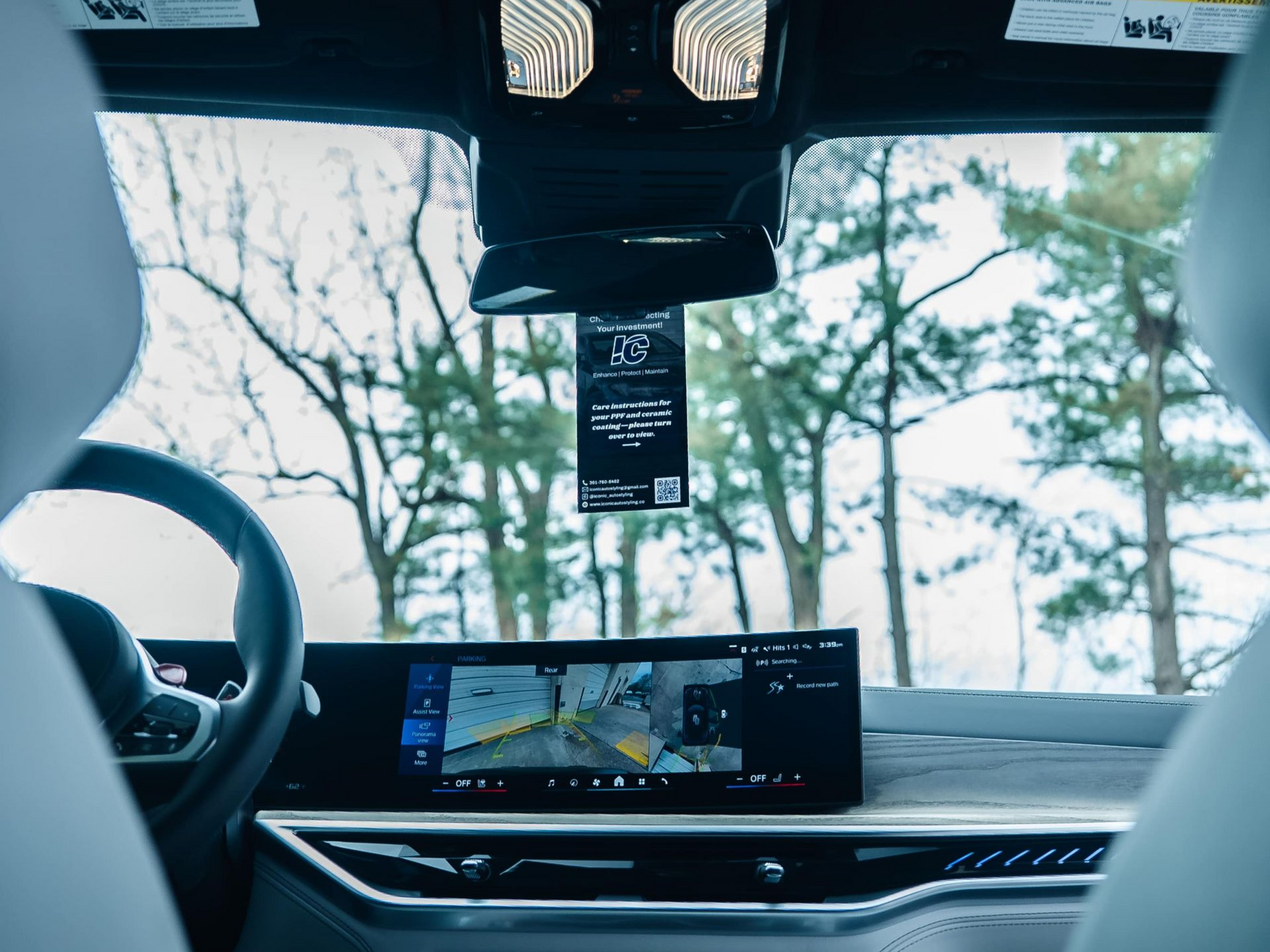 Interior view of a car looking out at trees, dashboard with screen displaying a camera view.