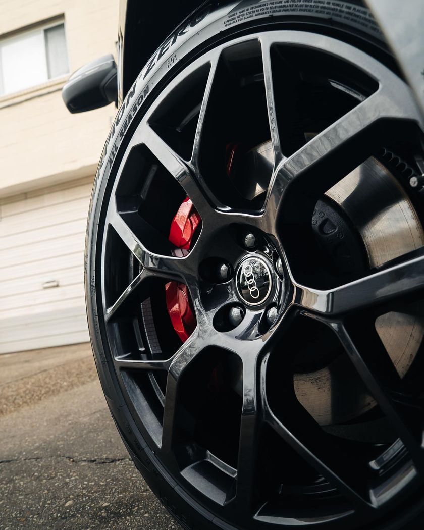 Black car wheel with red brake calipers; Audi logo on hubcap.