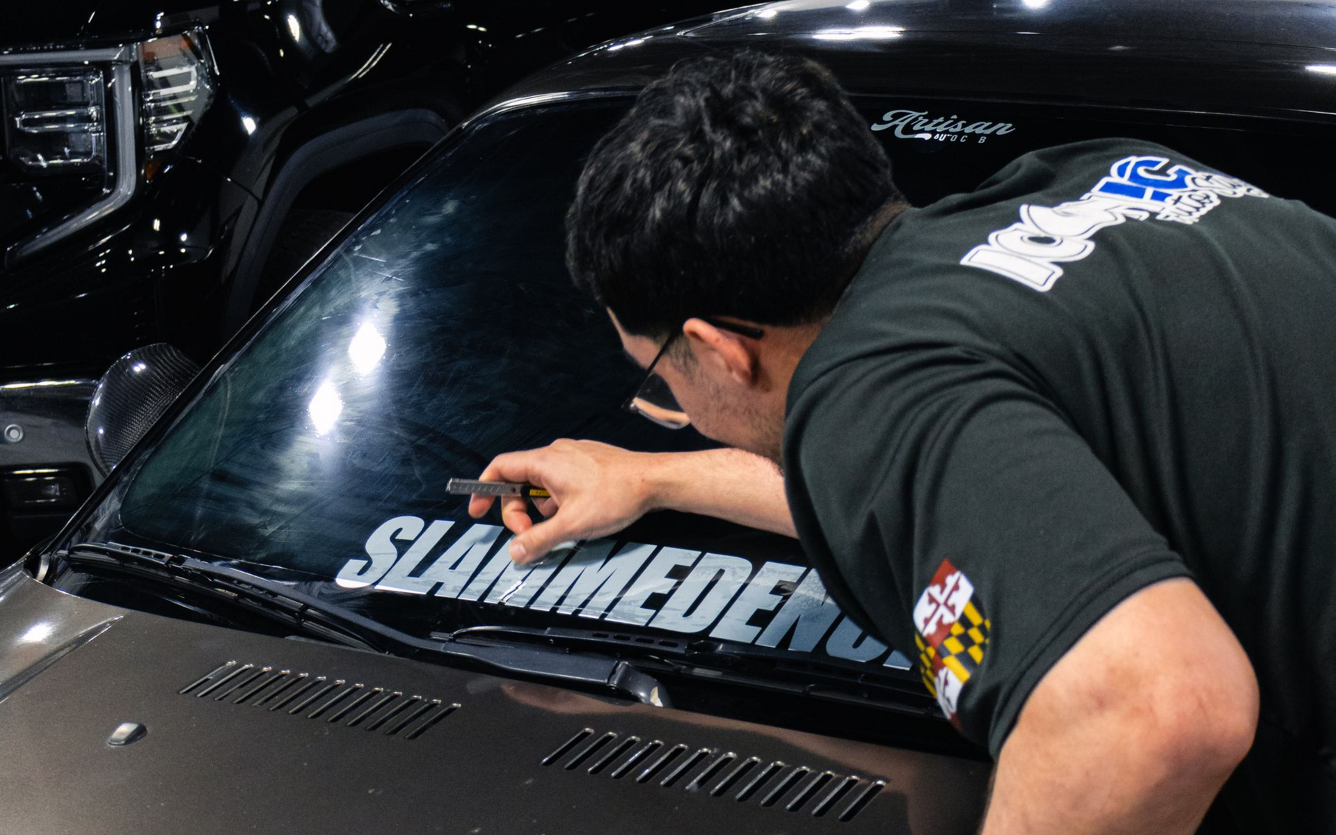 Person applying black vinyl lettering on a white wall. The person wears a black shirt.