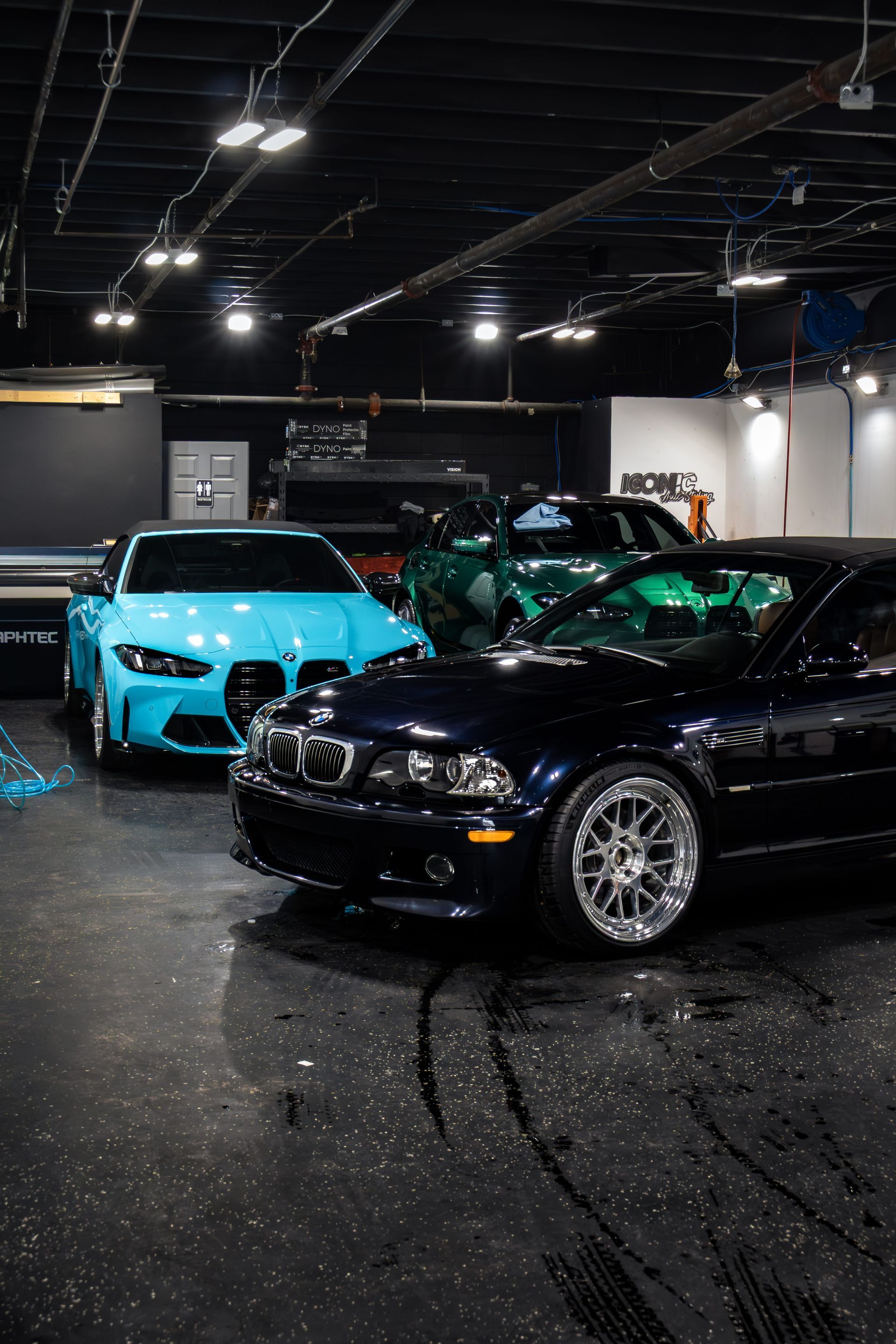 A dark blue E46 BMW M3 and a bright blue G80 BMW M3 parked inside a dimly lit garage.