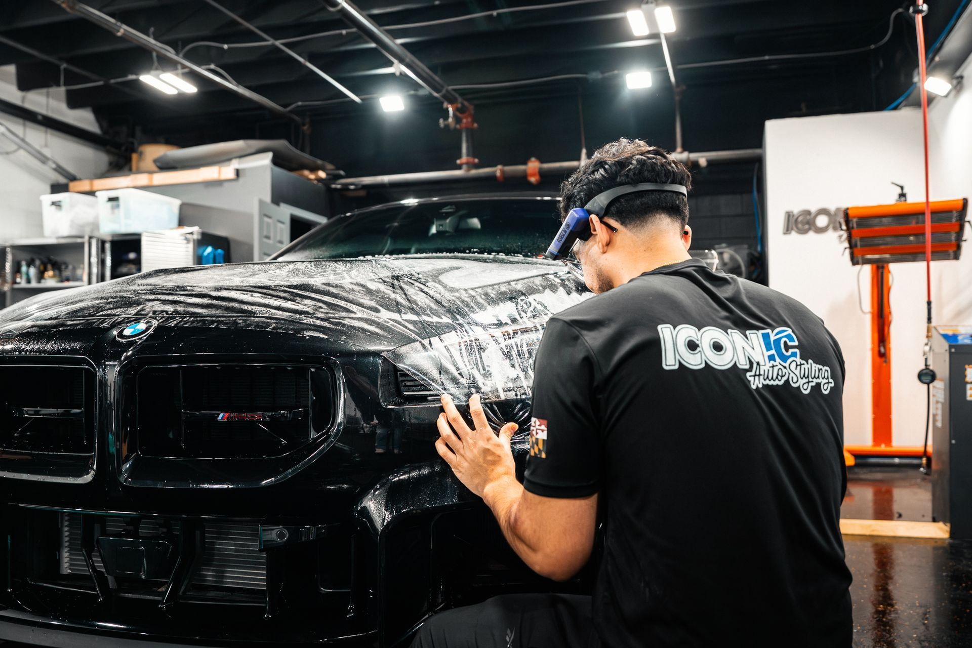 Dark gray BMW car hood reflecting a honeycomb pattern in a garage setting.