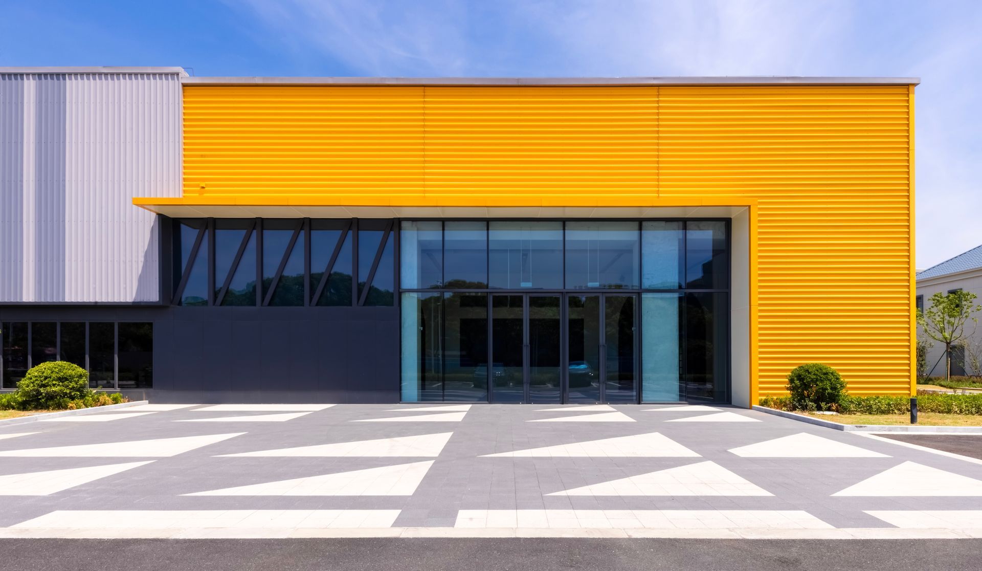 Yellow and gray modern building with glass doors and a patterned walkway.