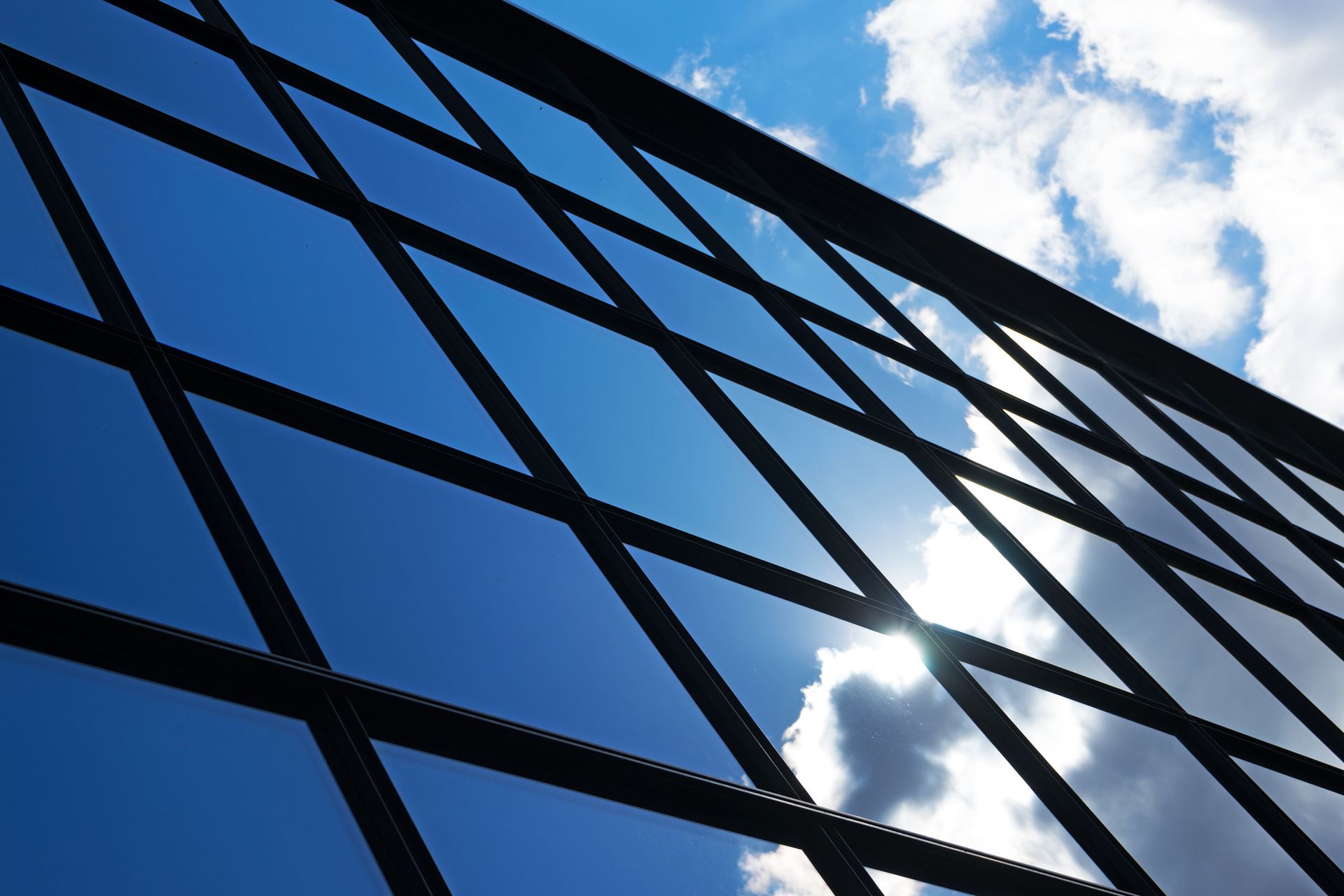 Black metal grid against a blue sky with fluffy white clouds, sun shining through.
