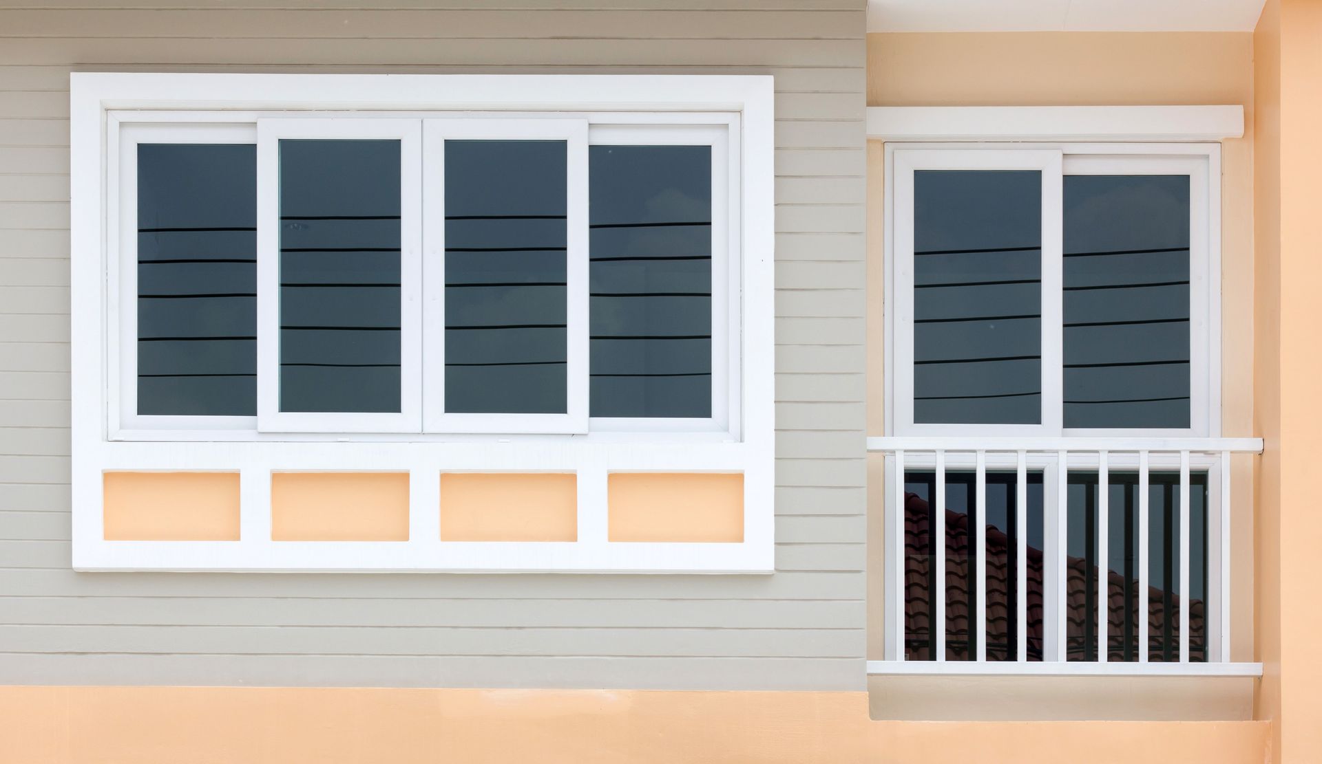 Two white-framed sliding windows on a building with a light gray and peach-colored facade.
