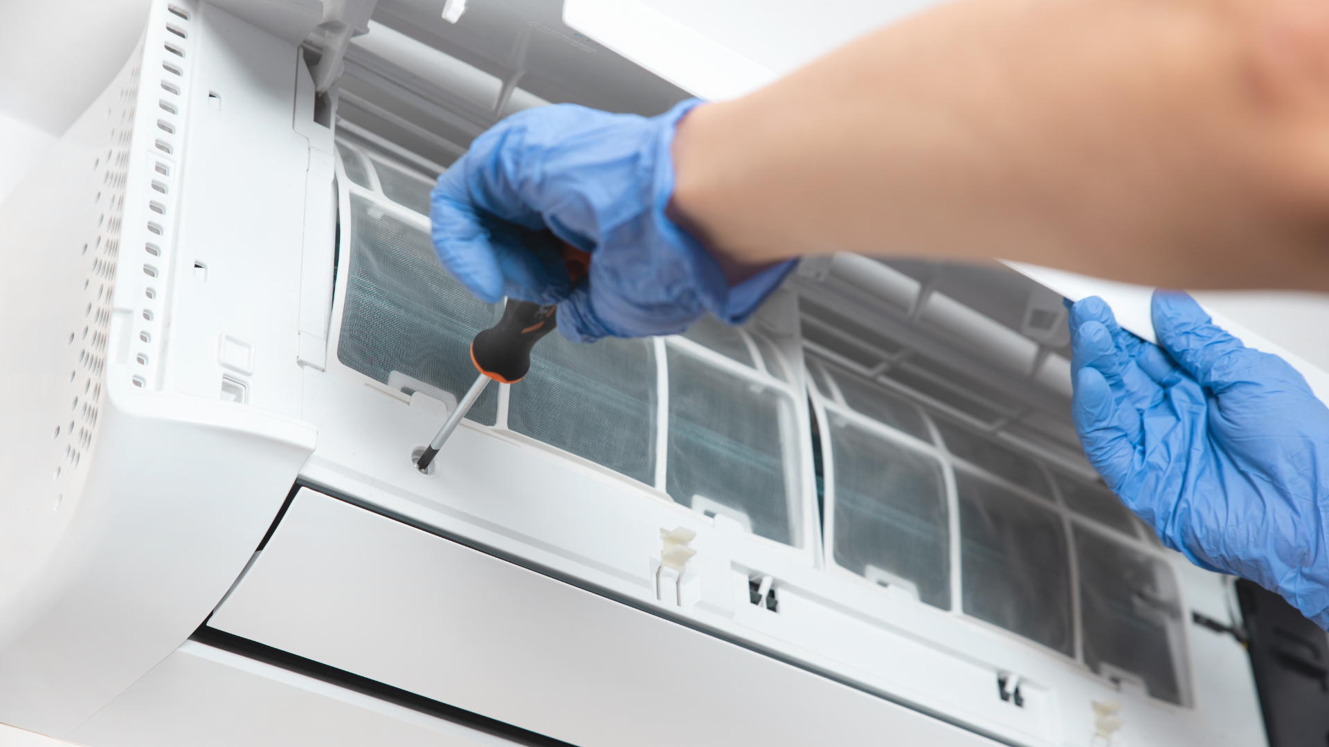 A person wearing blue gloves is fixing an air conditioner with a screwdriver.