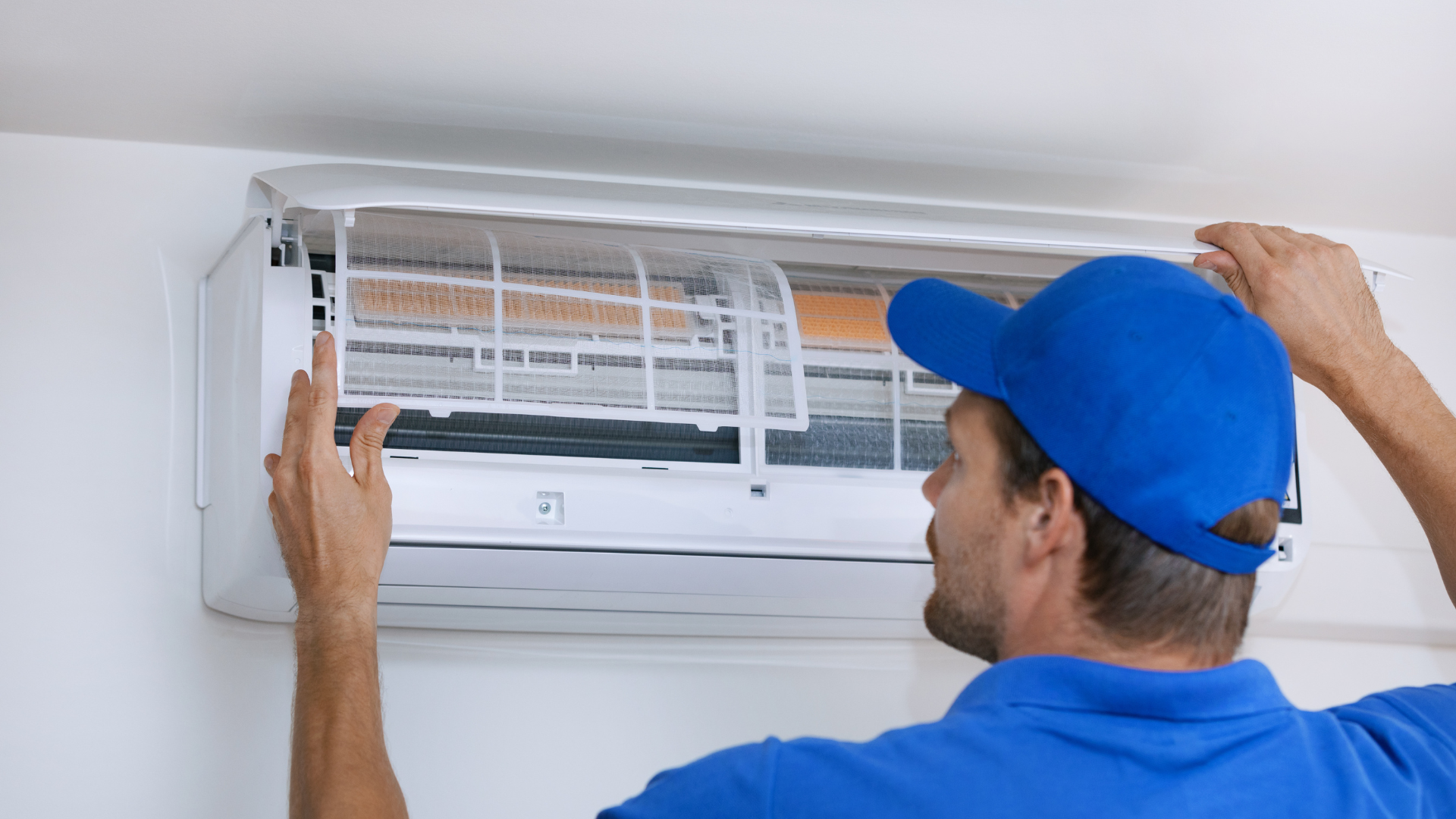 A man in a blue hat is cleaning an air conditioner.