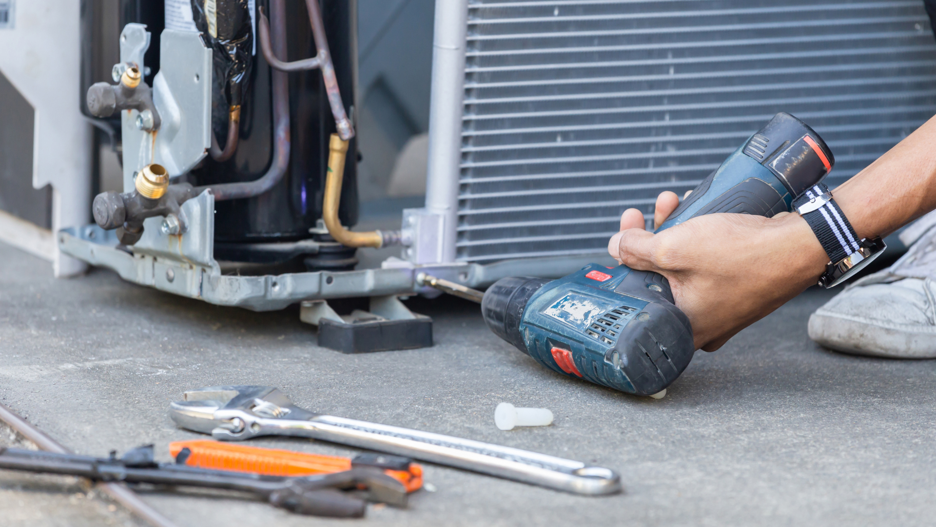 A person is fixing an air conditioner with a drill.