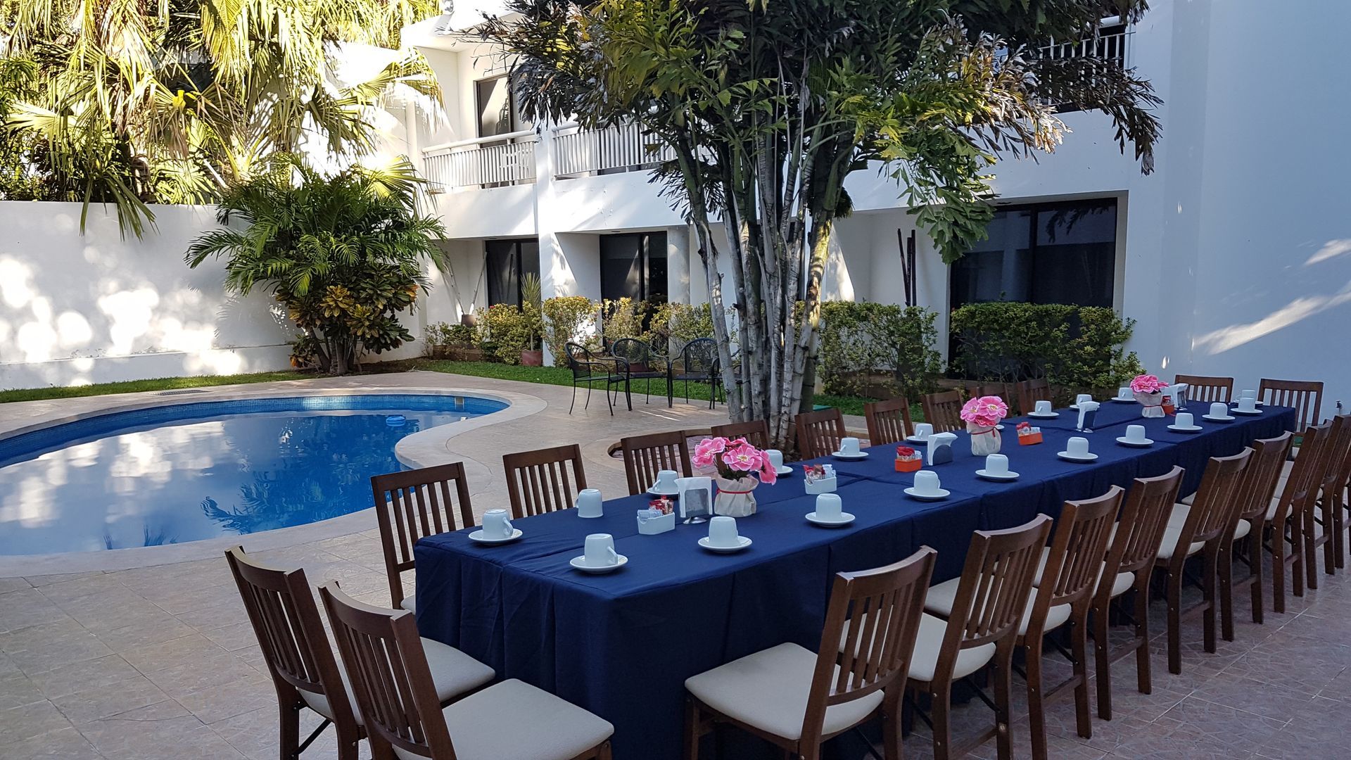 Una mesa larga con sillas frente a una piscina.