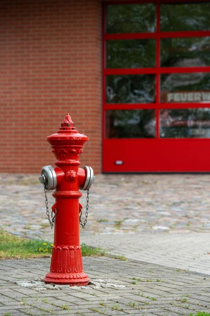 A red fire hydrant is sitting on the sidewalk in front of a fire station.