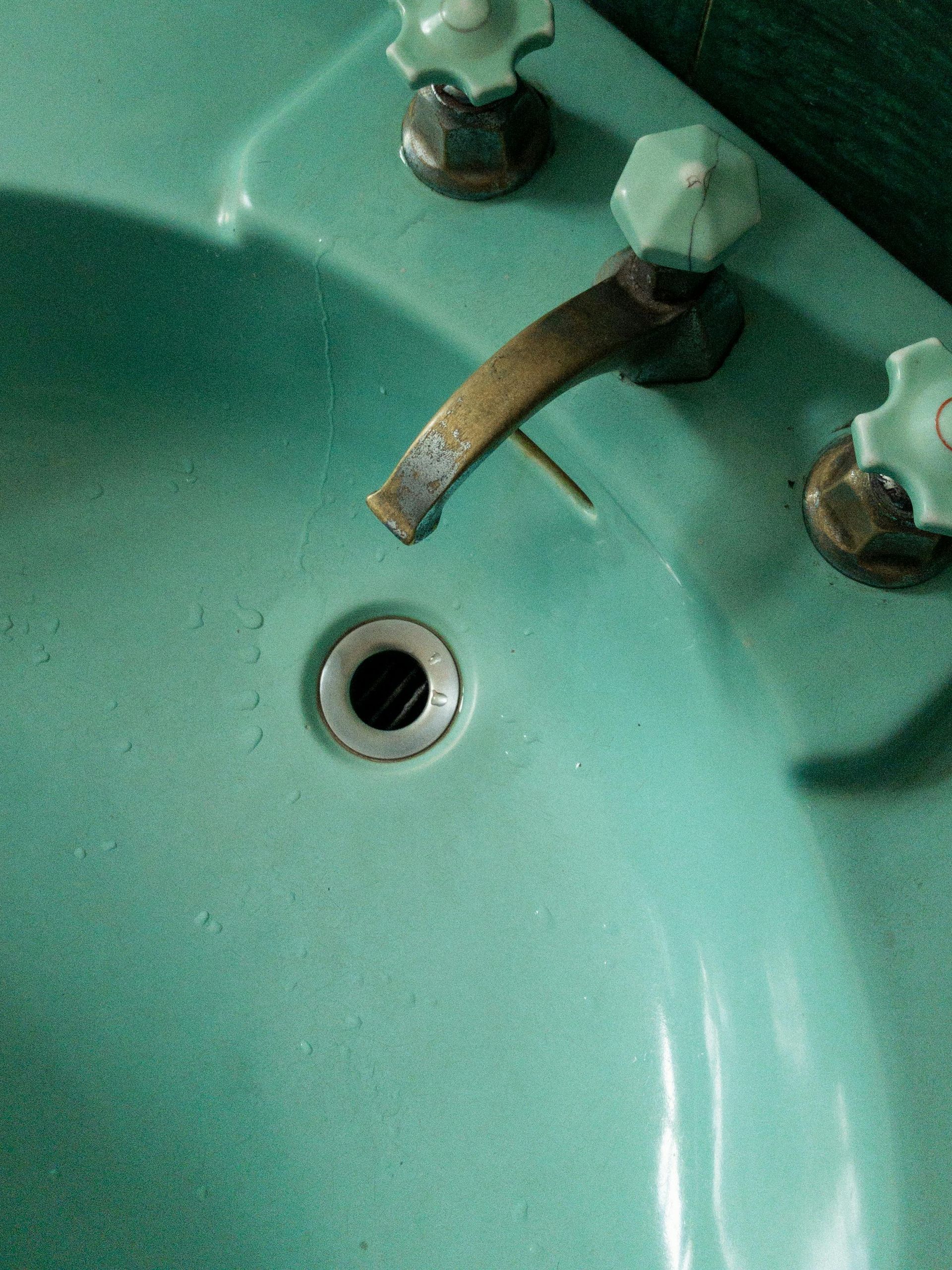 A bathroom sink with green handles and a drain hole.