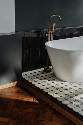 A bathroom with a bathtub and a faucet on a wooden floor.
