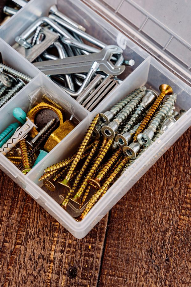 A plastic box filled with screws and wrenches on a wooden table.
