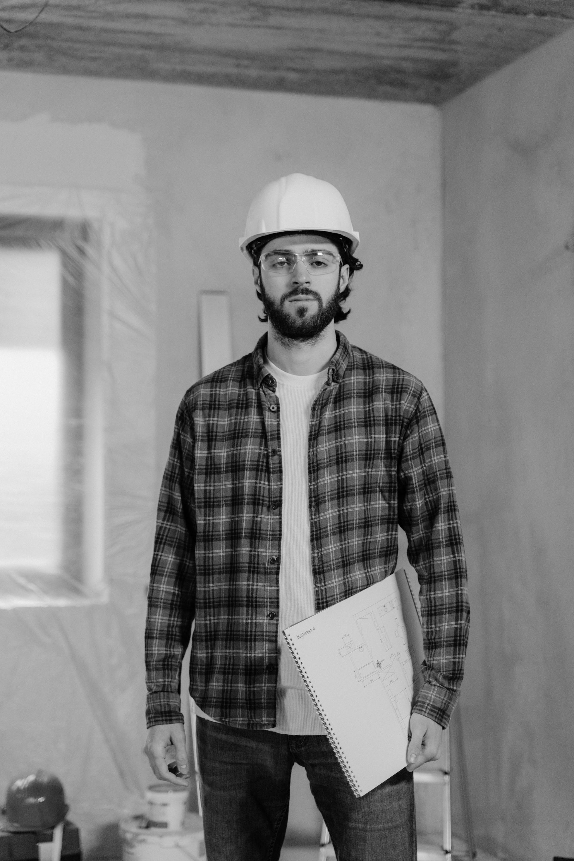 A man wearing a hard hat and a plaid shirt is holding a piece of paper.