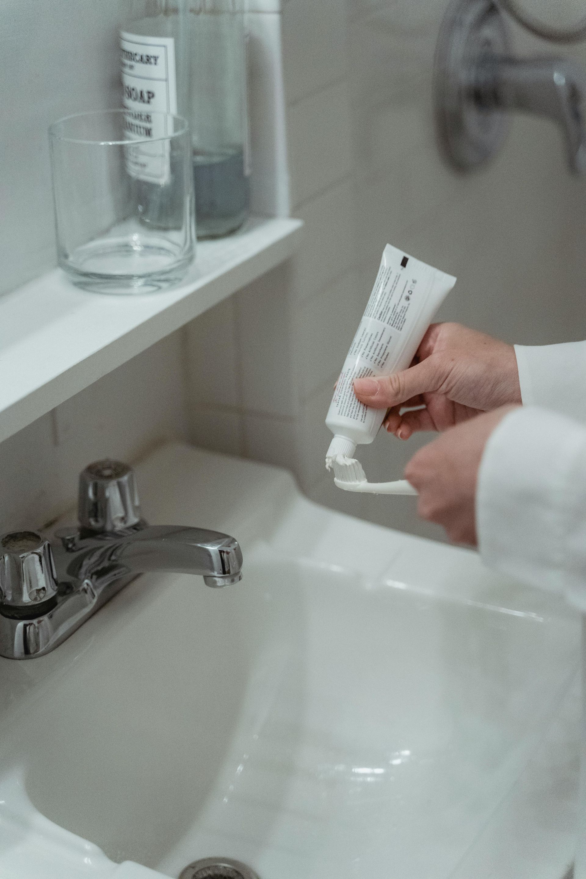 A person is putting toothpaste on a toothbrush in a bathroom sink.