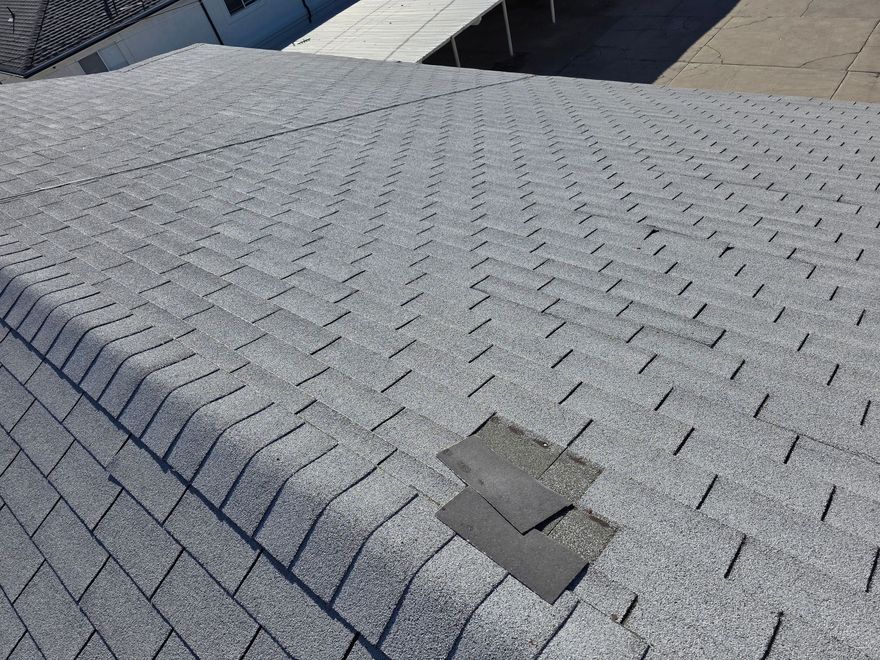 Overhead view of a gray shingle roof with two displaced shingles in the center.