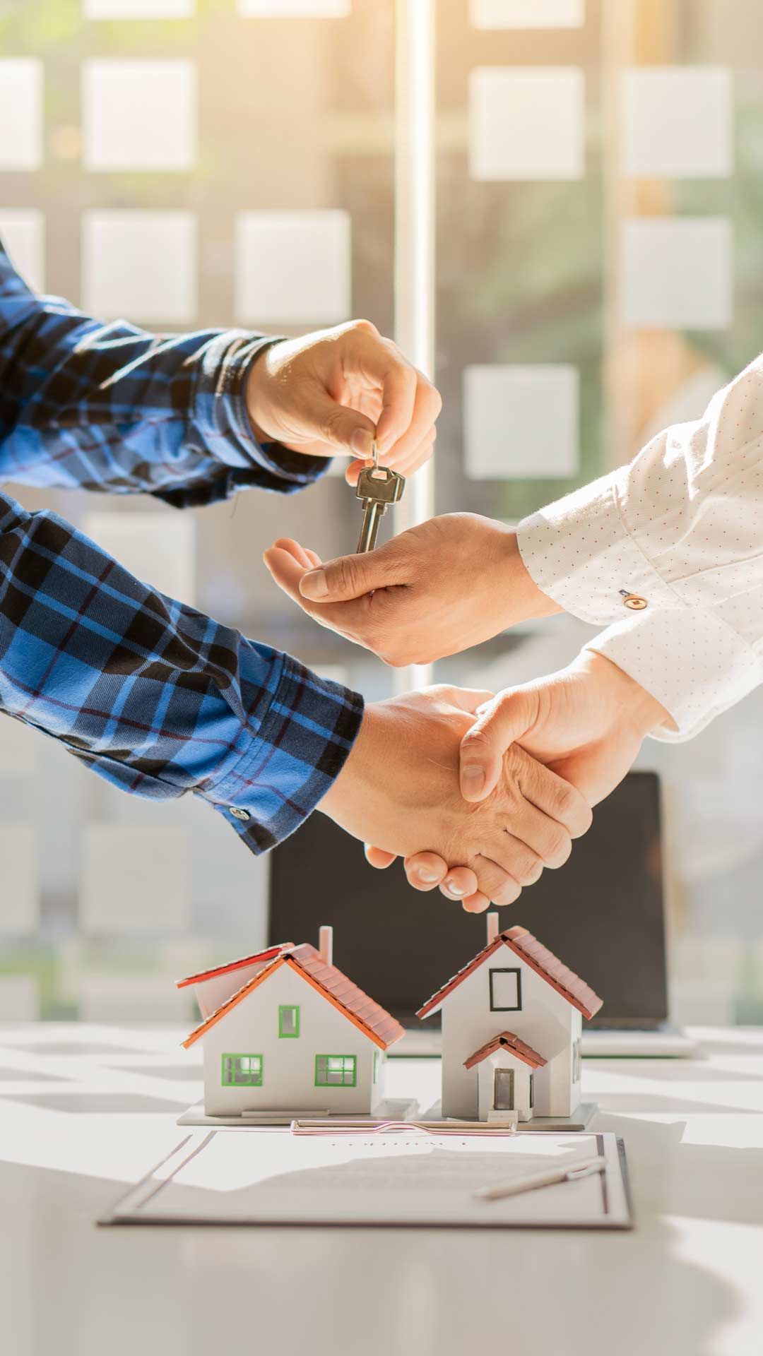 A man is handing a key to another man while shaking hands.