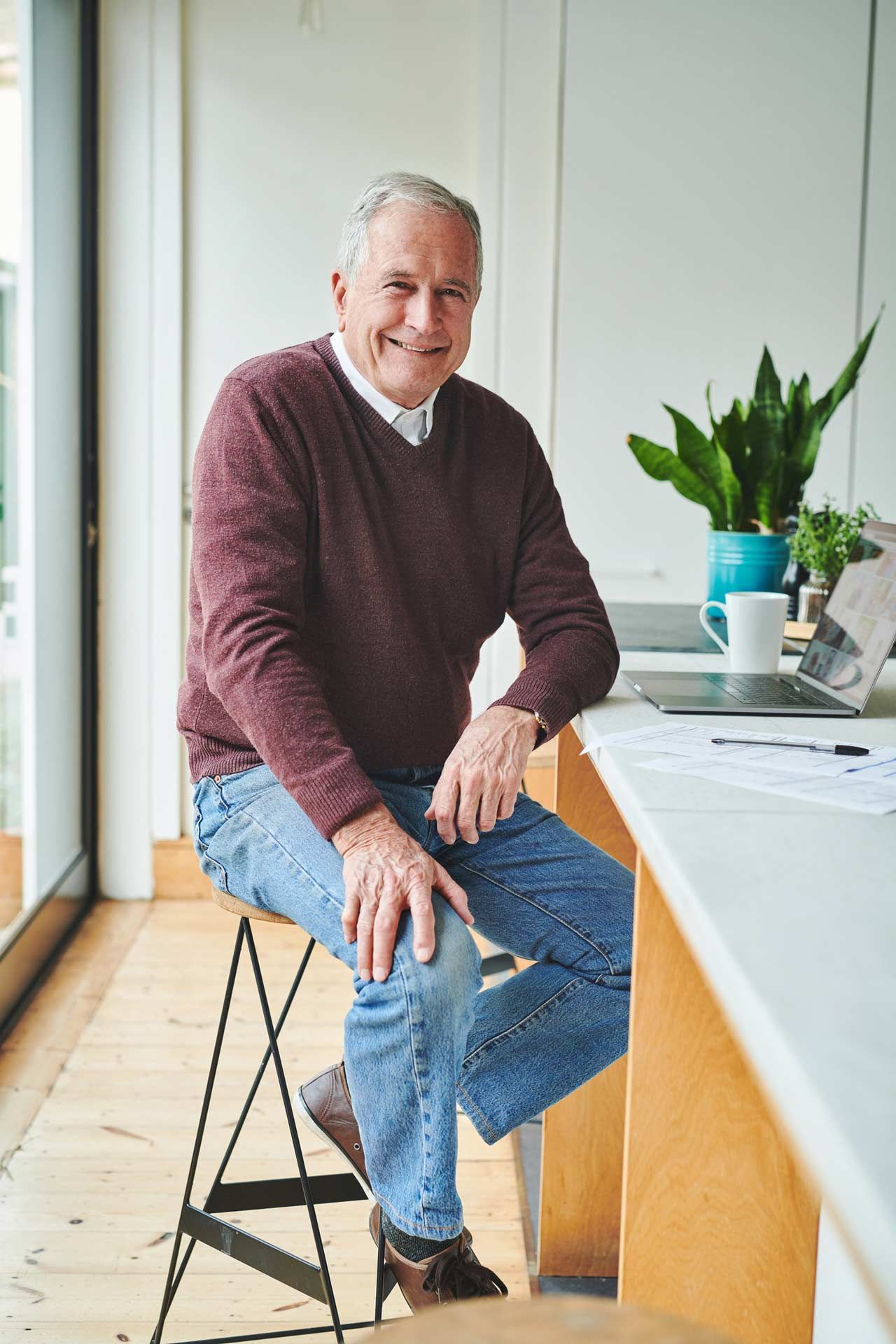A man is sitting on a stool in front of a laptop computer.