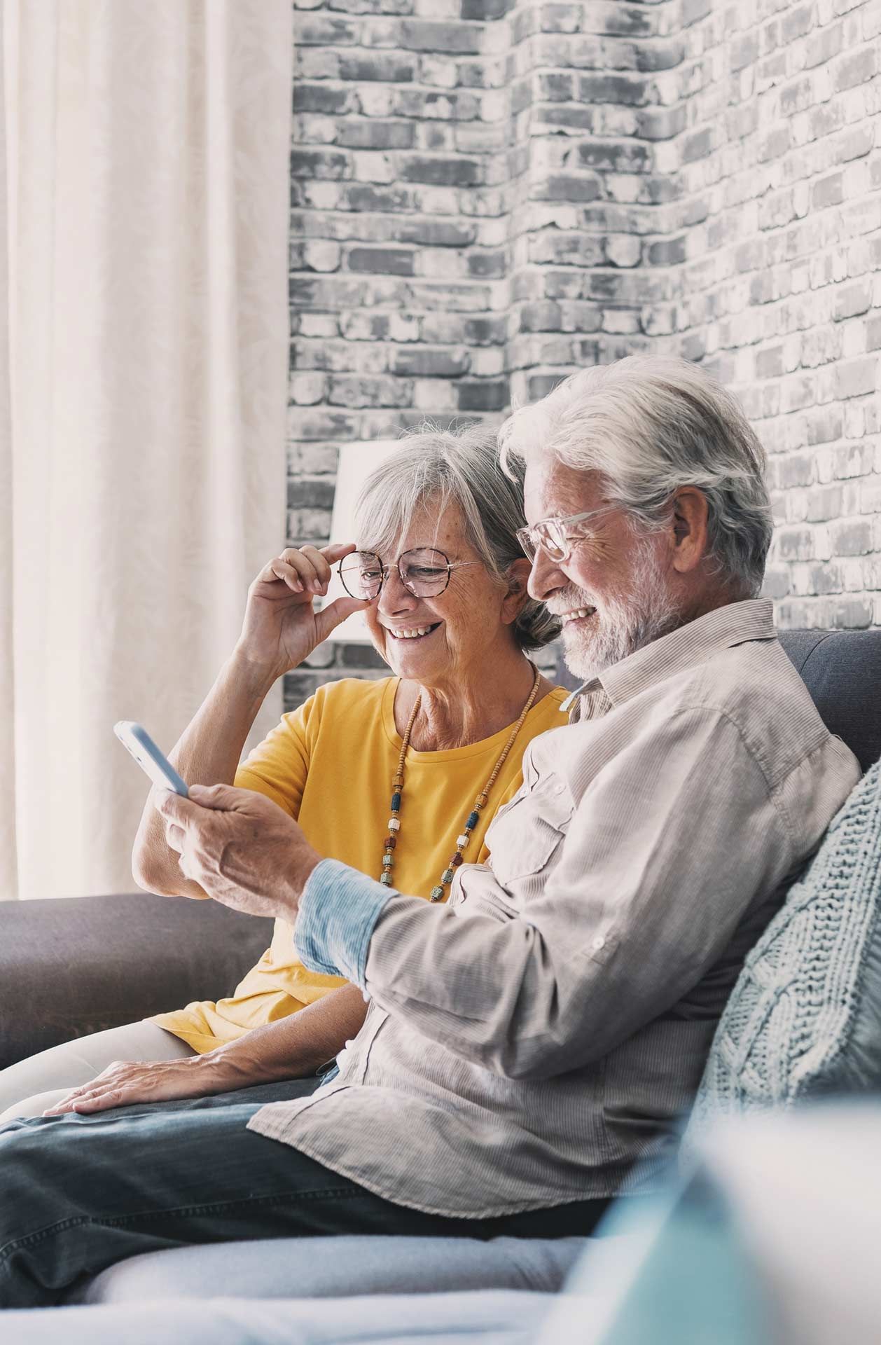 An elderly couple is sitting on a couch looking at a cell phone.