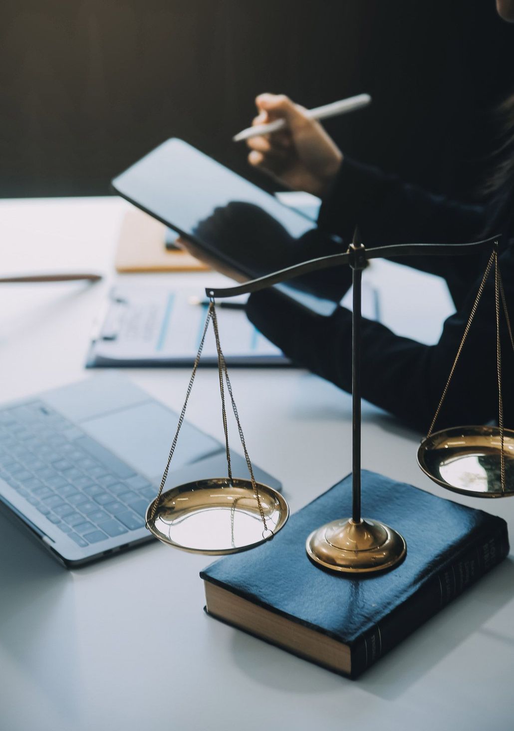 A person is using a tablet next to a book and scales of justice.