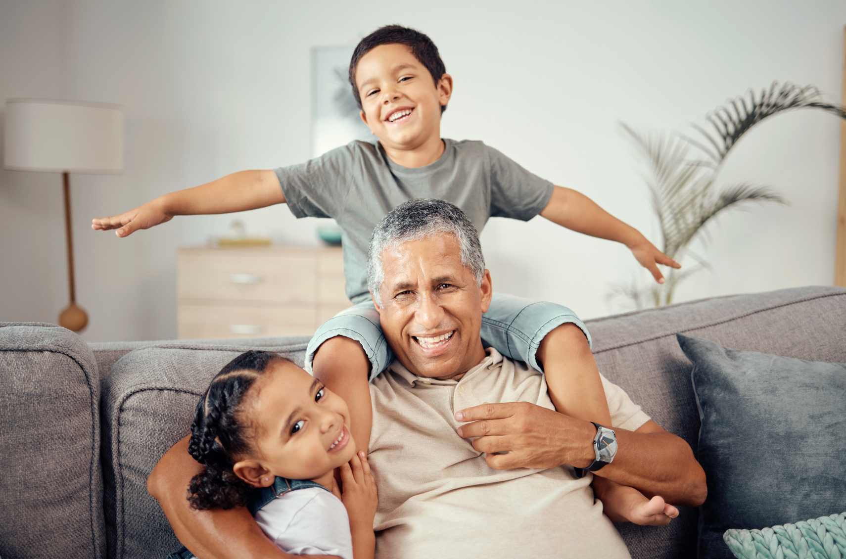Grandpa sitting on the couch with his two grandkids smiling at the camera, indicating reverse mortgage specialist near Aurora