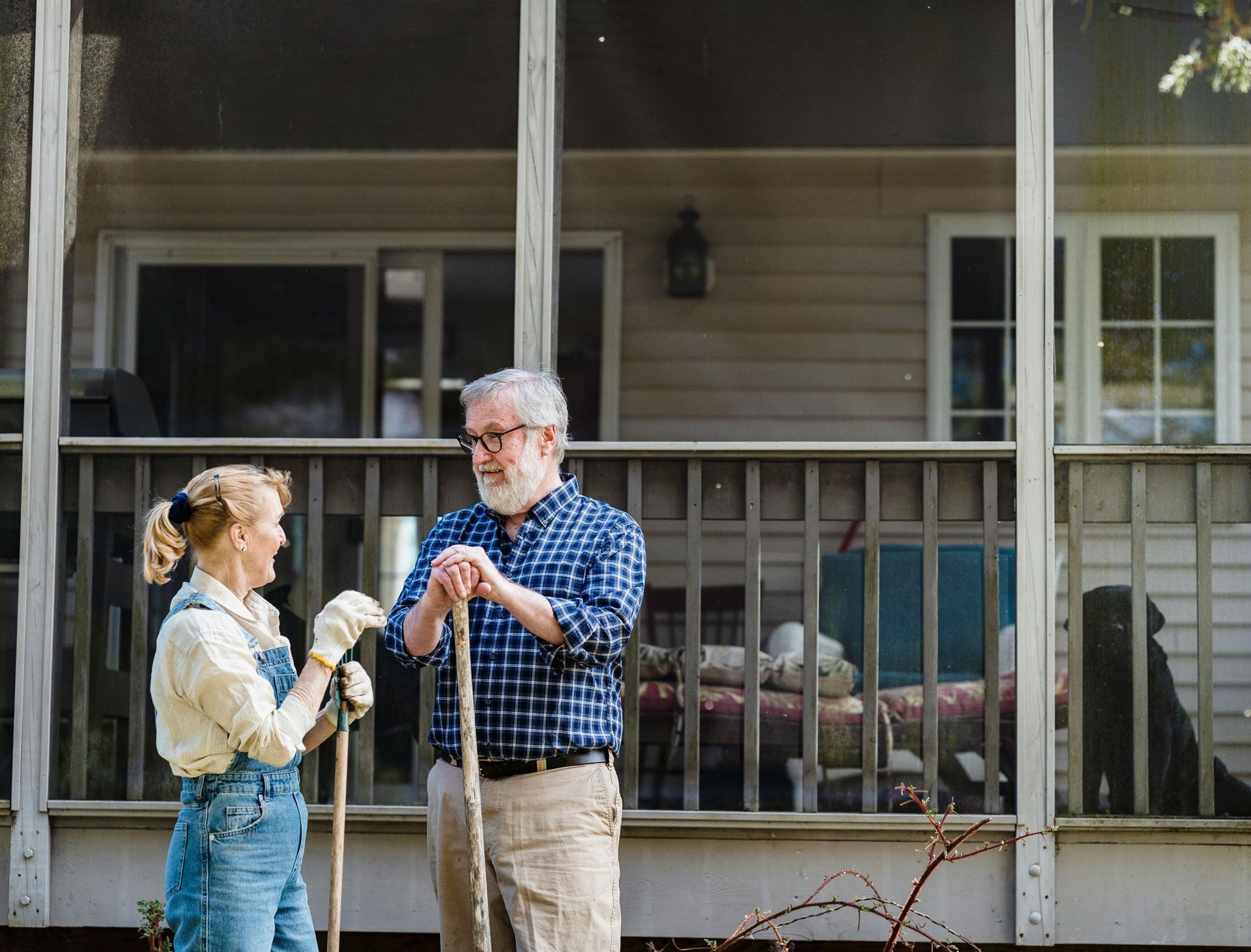 Couple gardening together, talking. House with porch in background.