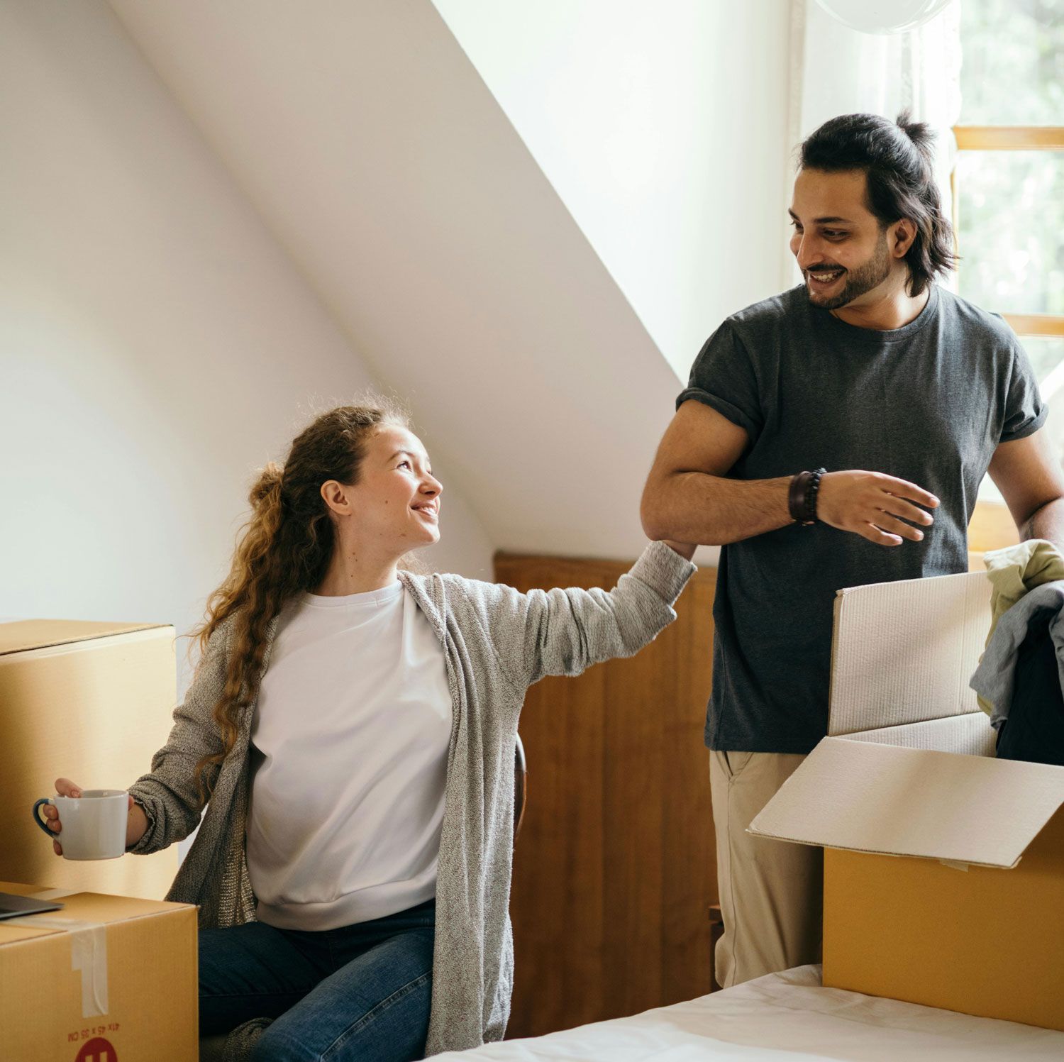 Couple unpacking boxes in a bright room, smiling and looking at each other.