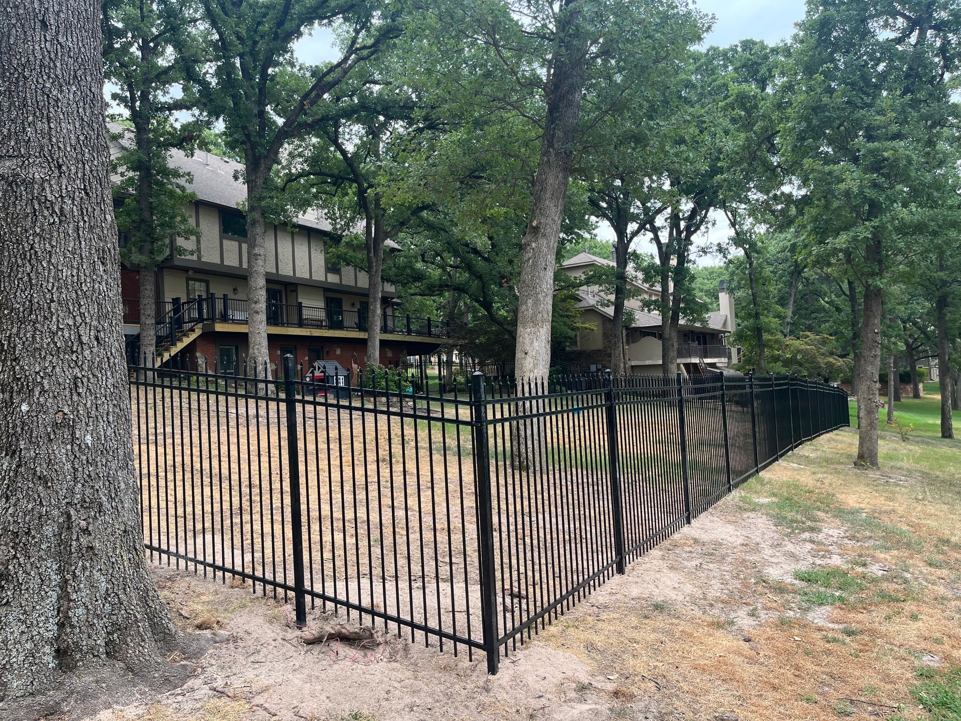 A black wrought iron fence is surrounded by trees in front of a house.
